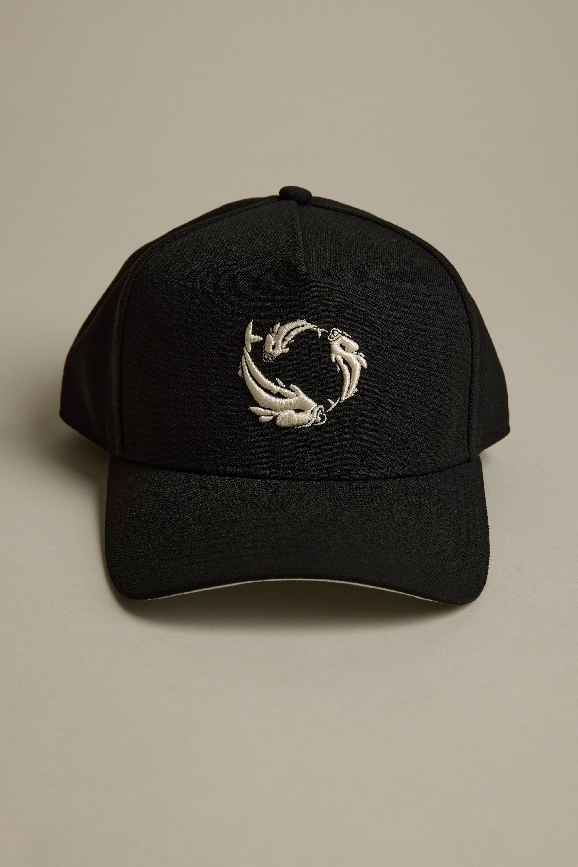 The Legasea Logo Snapback Cap by Legasea is a black adjustable hat featuring an embroidered design of three koi fish swimming in a circular pattern on the front, shown against a neutral background.