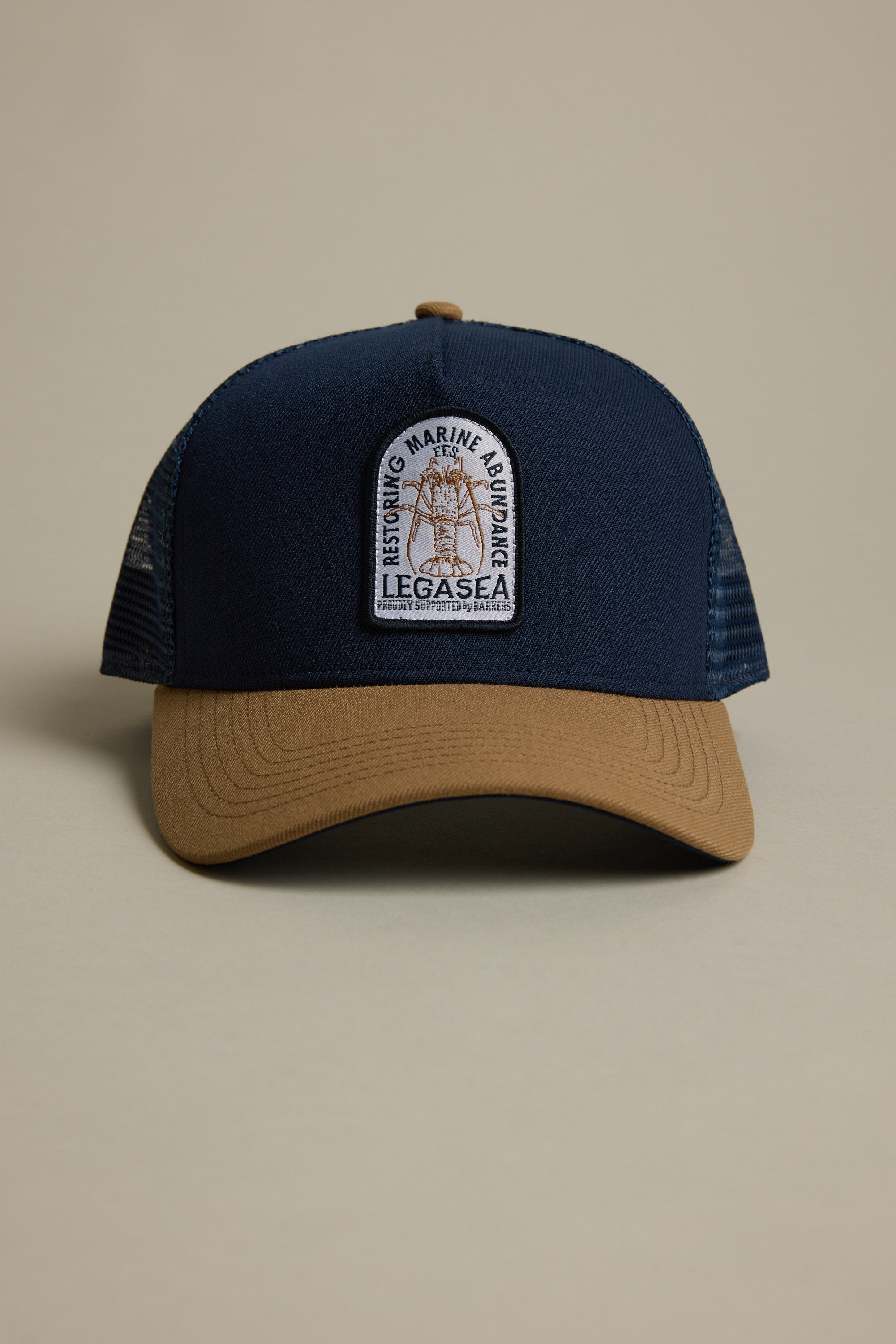The Legasea Crayfish Trucker Snapback Cap by Legasea is a navy blue and tan adjustable mesh-back hat with an F.F.S. patch reading “Restoring Marine Abundance, LegaSea,” featuring a fish graphic, shown on a neutral background.