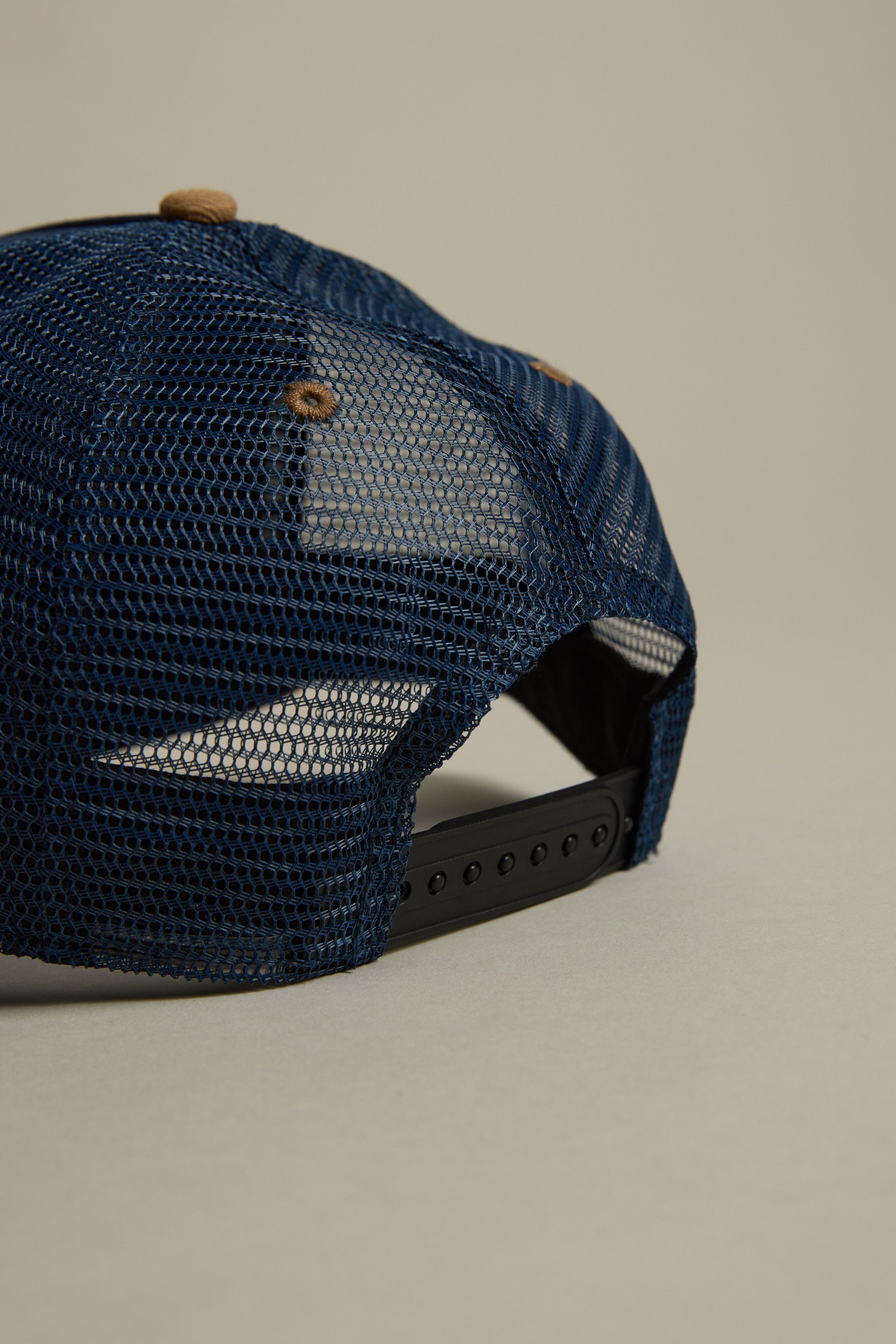 A close-up of the back of the Legasea Crayfish Trucker Snapback Cap by Legasea, featuring blue mesh, a black adjustable strap, and brown button details against a neutral background.