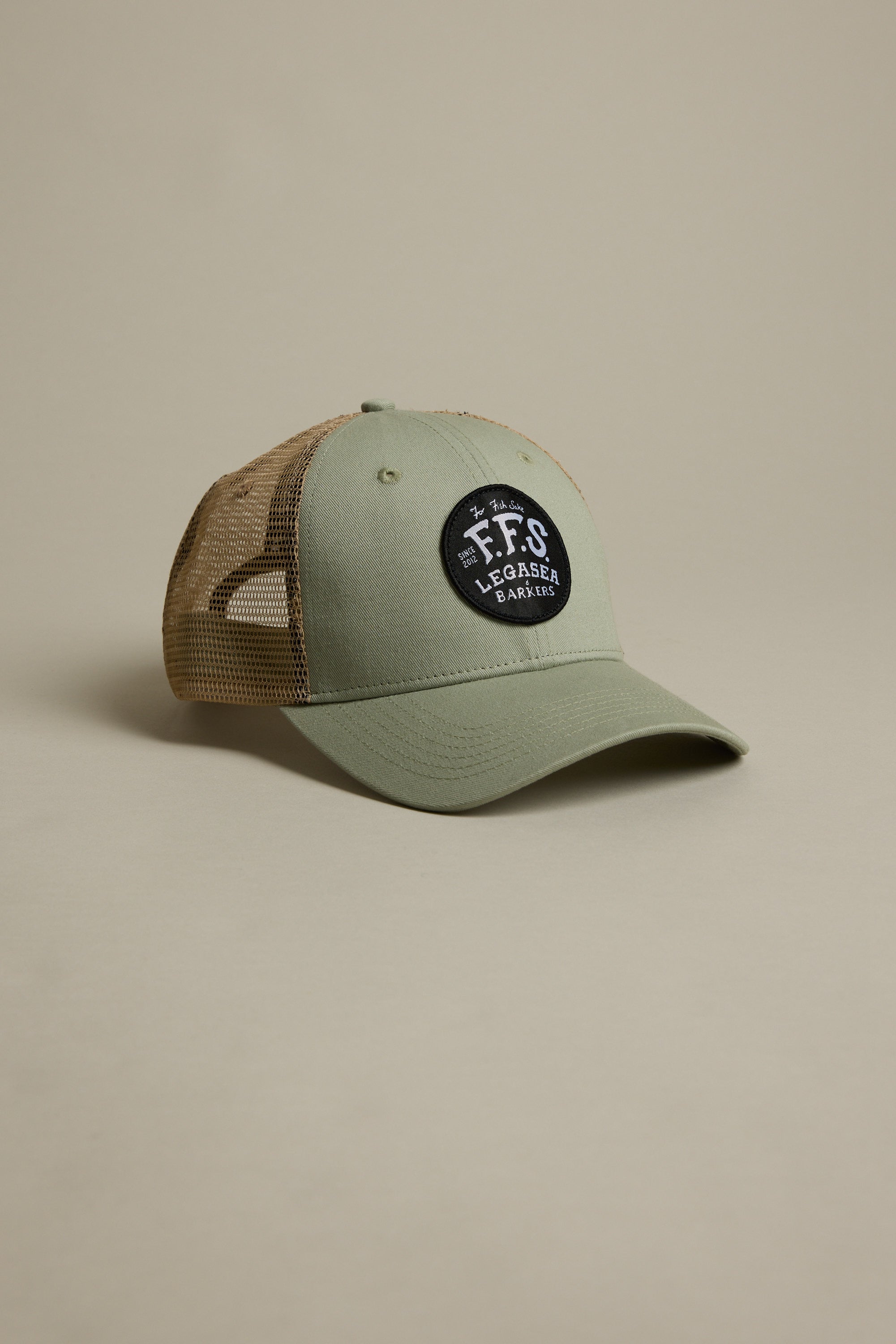 The Legasea FFS Trucker Cap features green and tan mesh with a black patch that reads "FFS Legacy Eager" in white. Displayed on a beige background, it's perfect for Legasea fans.