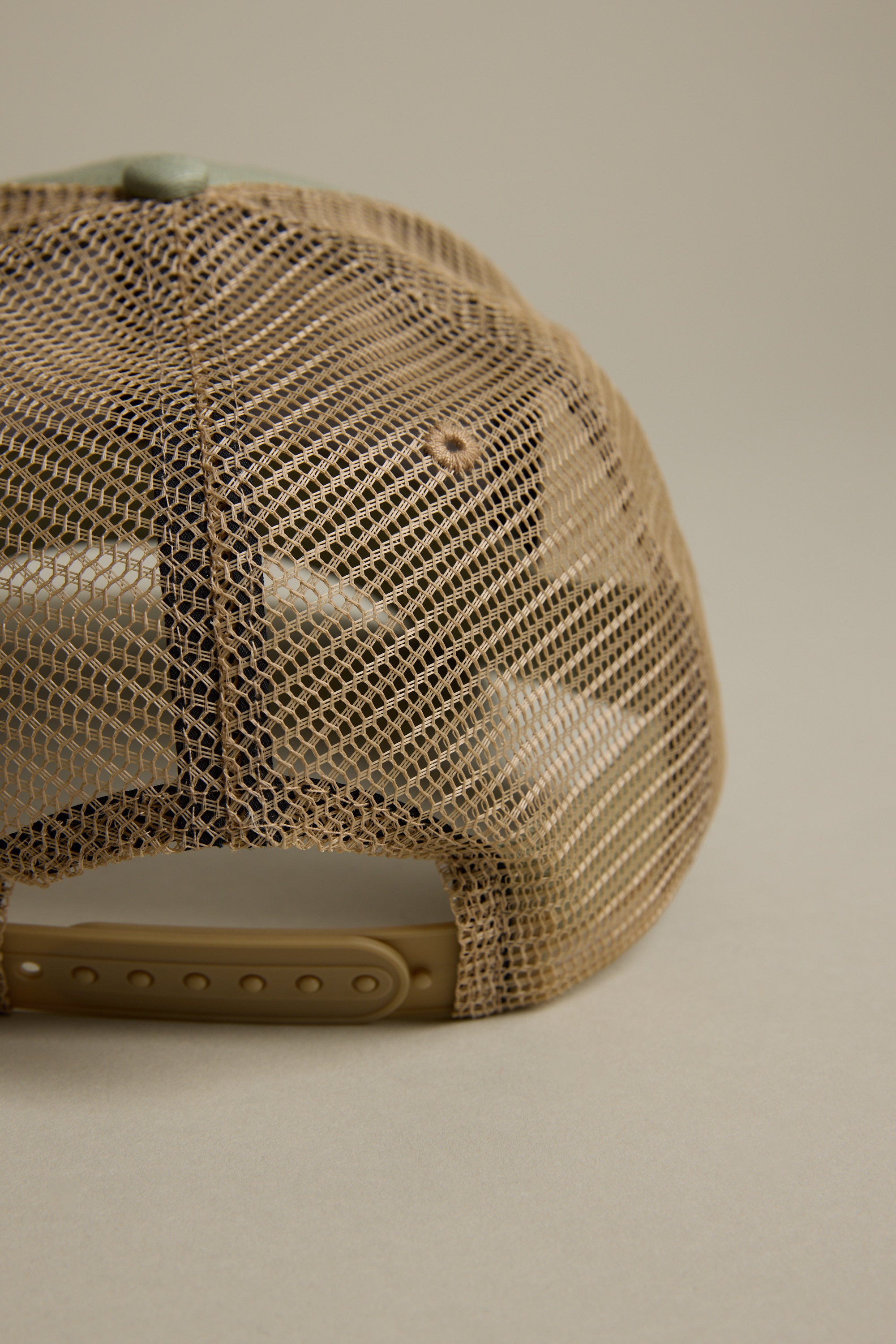 Close-up of the back of the tan mesh Legasea FFS Trucker Cap by Legasea, featuring an adjustable snapback strap against a neutral background. This classic trucker hat is ideal for fans of the Legasea collection.