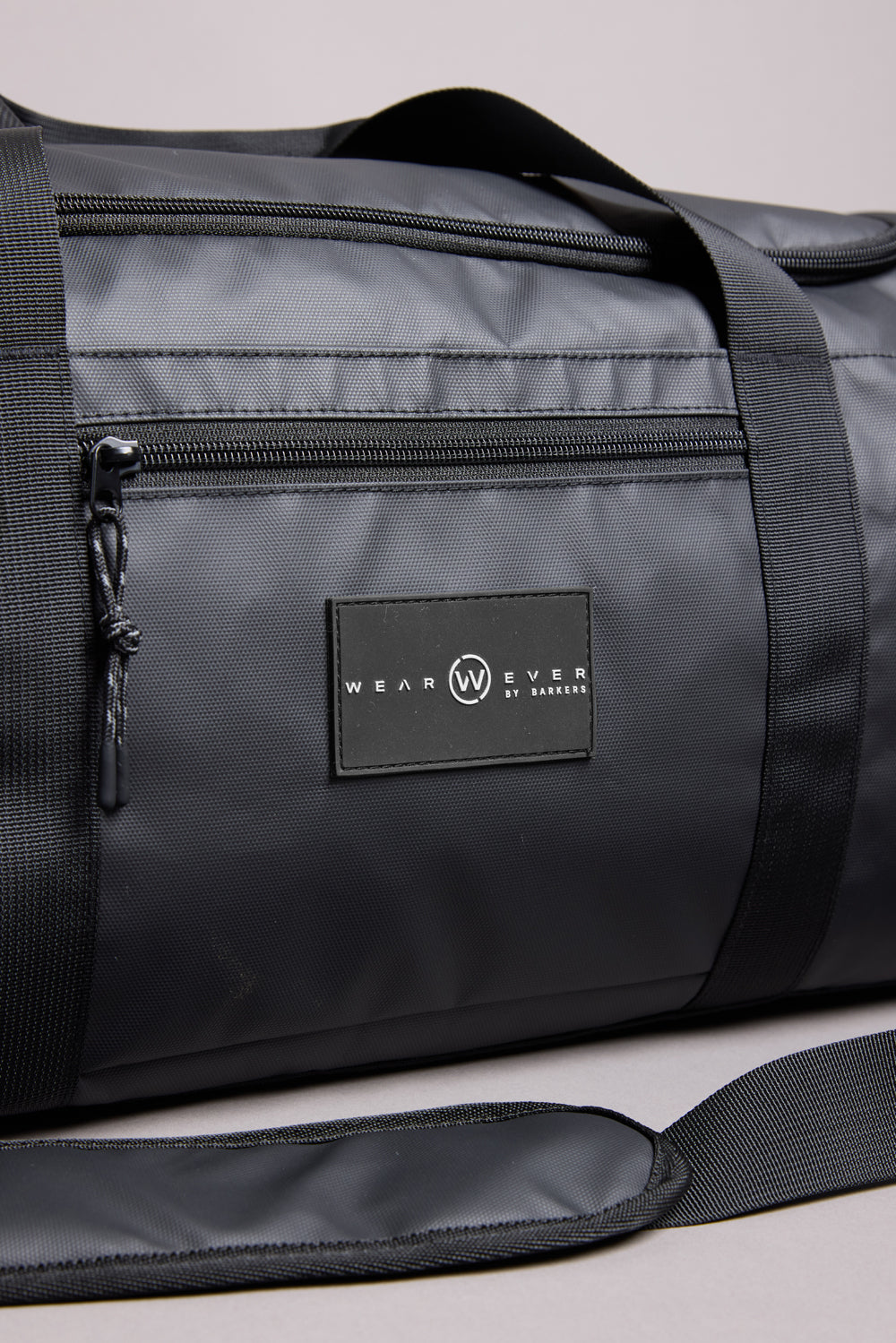 A close-up of the WearEver Transit Holdall, a black, water-resistant duffel bag with a zipper pocket, shoulder strap, visible stitching, WEAR EVER BY LAMAR label in white, and a convenient sneaker pocket.