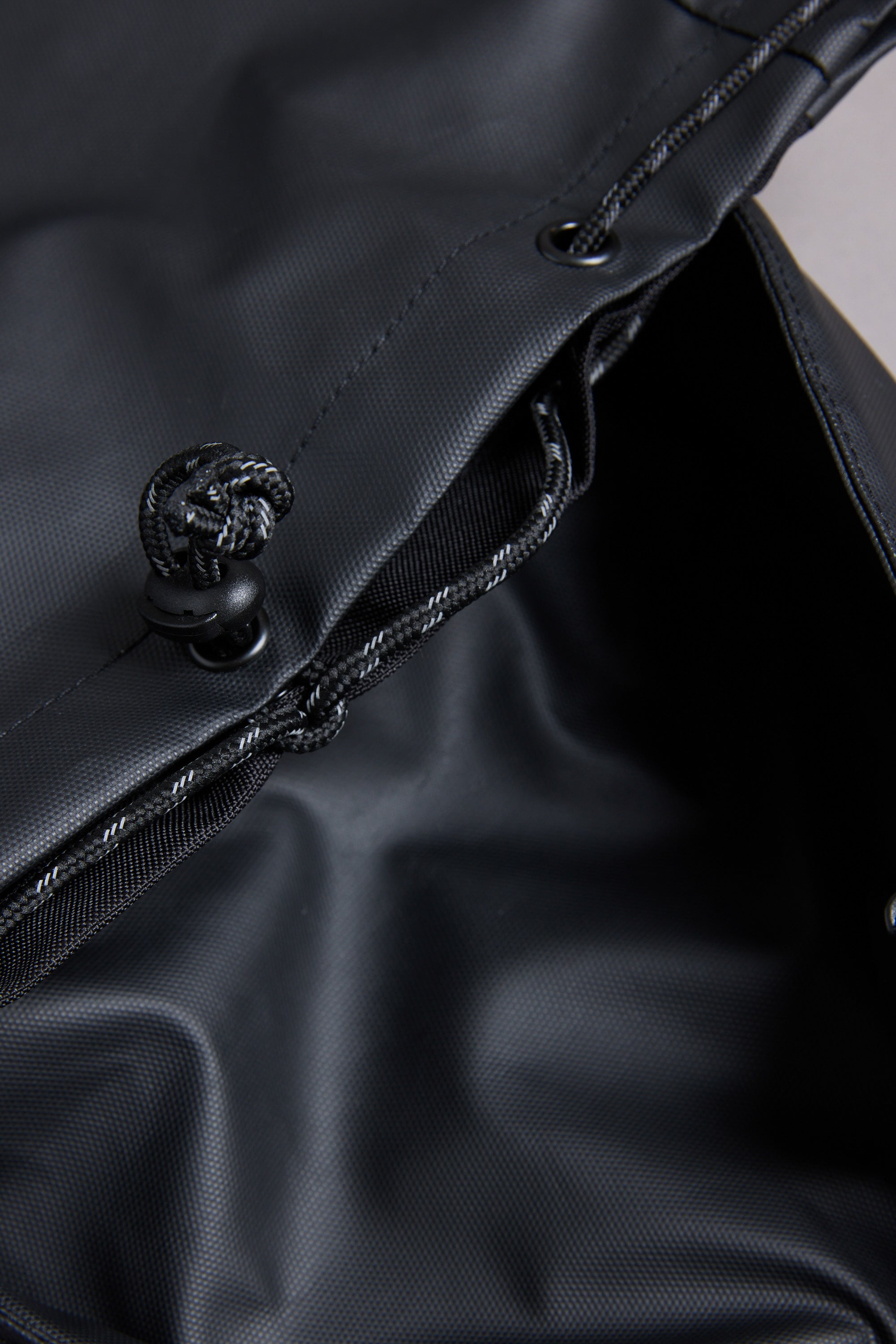 Close-up of the WearEver Transit Backpack’s black drawstring bag, showing water-resistant zips, textured synthetic fabric, and an open top with a visible cord and cinch mechanism.