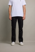 Person in a white t-shirt, Barkers Wanderer Denim Straight Jean, and sneakers stands against background.