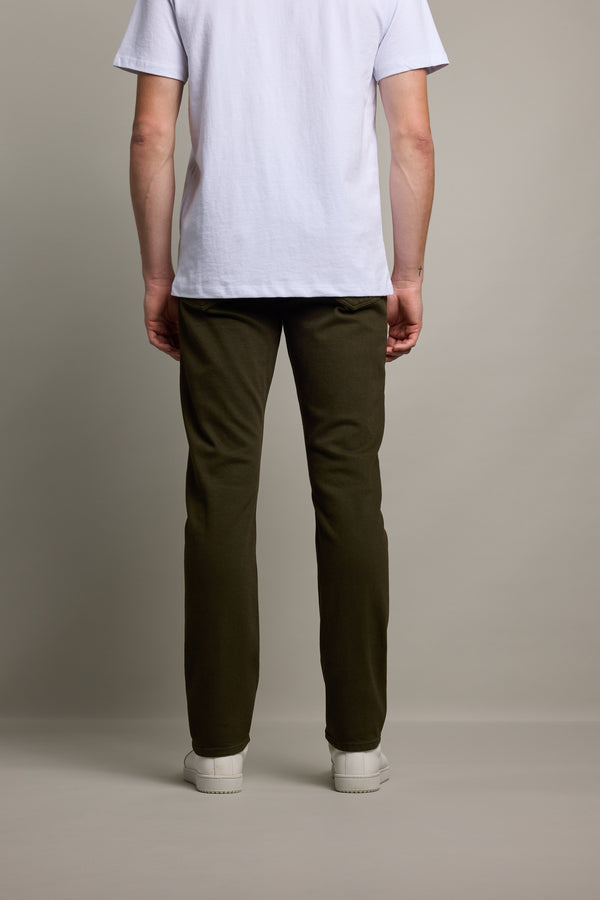 A person stands facing away from the camera, wearing a white short-sleeve t-shirt and Barkers Rambler Slim Coloured Jeans, paired with white sneakers against a plain light-colored background.