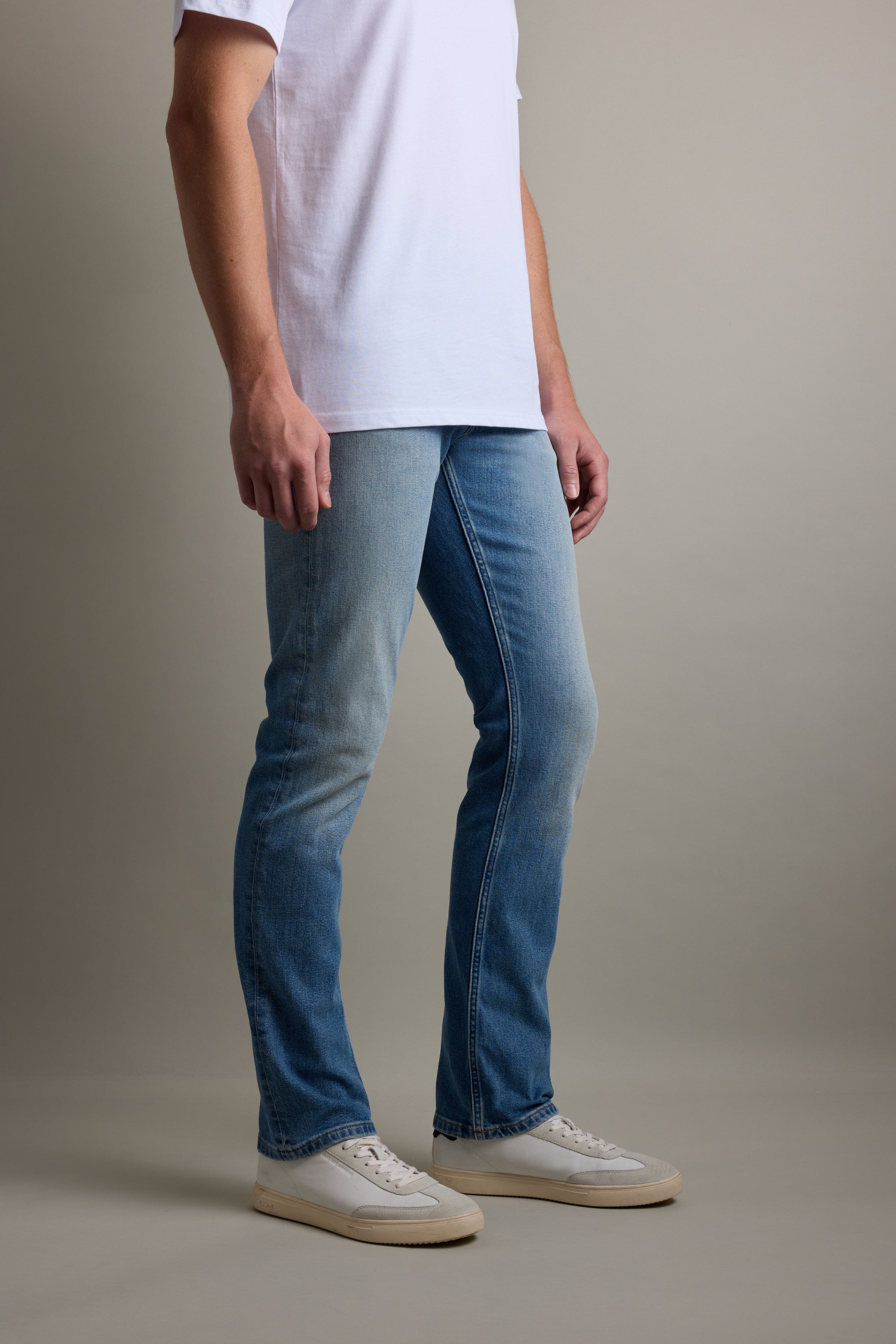Person in Barkers Wanderer Denim Straight Jean, white shirt, and sneakers against a neutral backdrop.