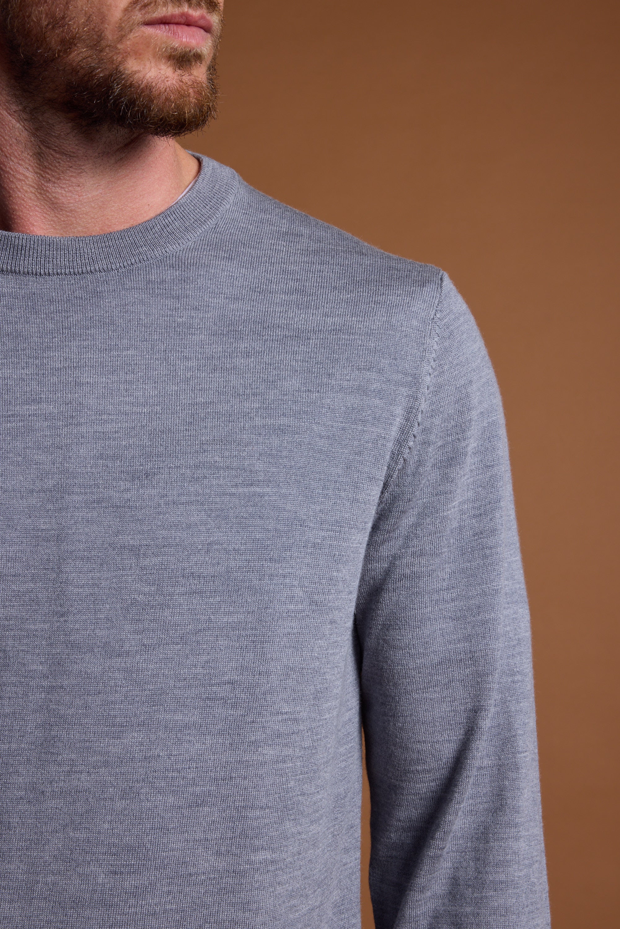 A man models the Barkers Skyland ZQrx Merino Crew in light gray, shown from the shoulders up with his head partly out of frame, set against a plain brown background.