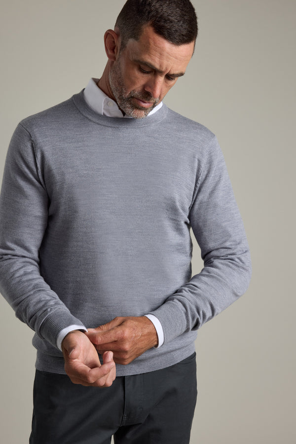 Man in a gray Barkers Skyland ZQrx Merino Crew sweater buttoning his cuff, looking down.