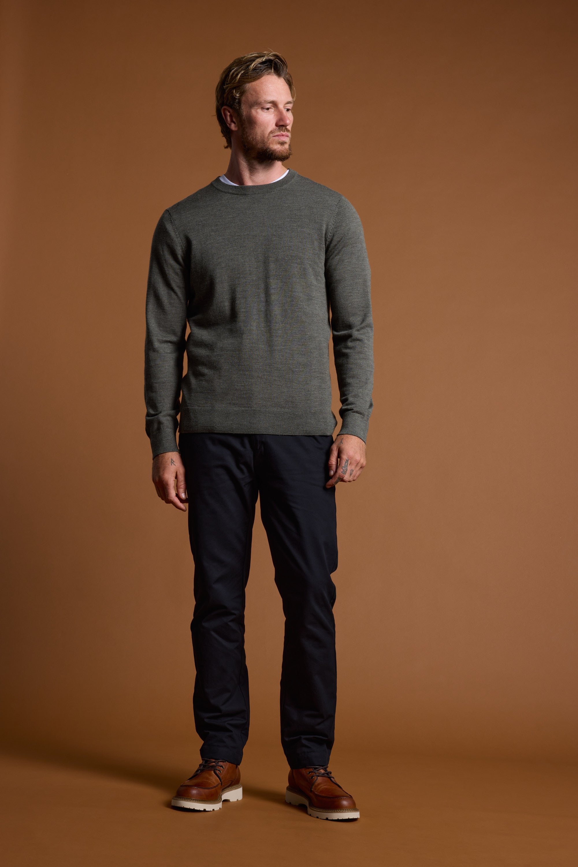 Man in Barkers Skyland ZQrx Merino Crew, dark pants, and brown shoes, brown backdrop.