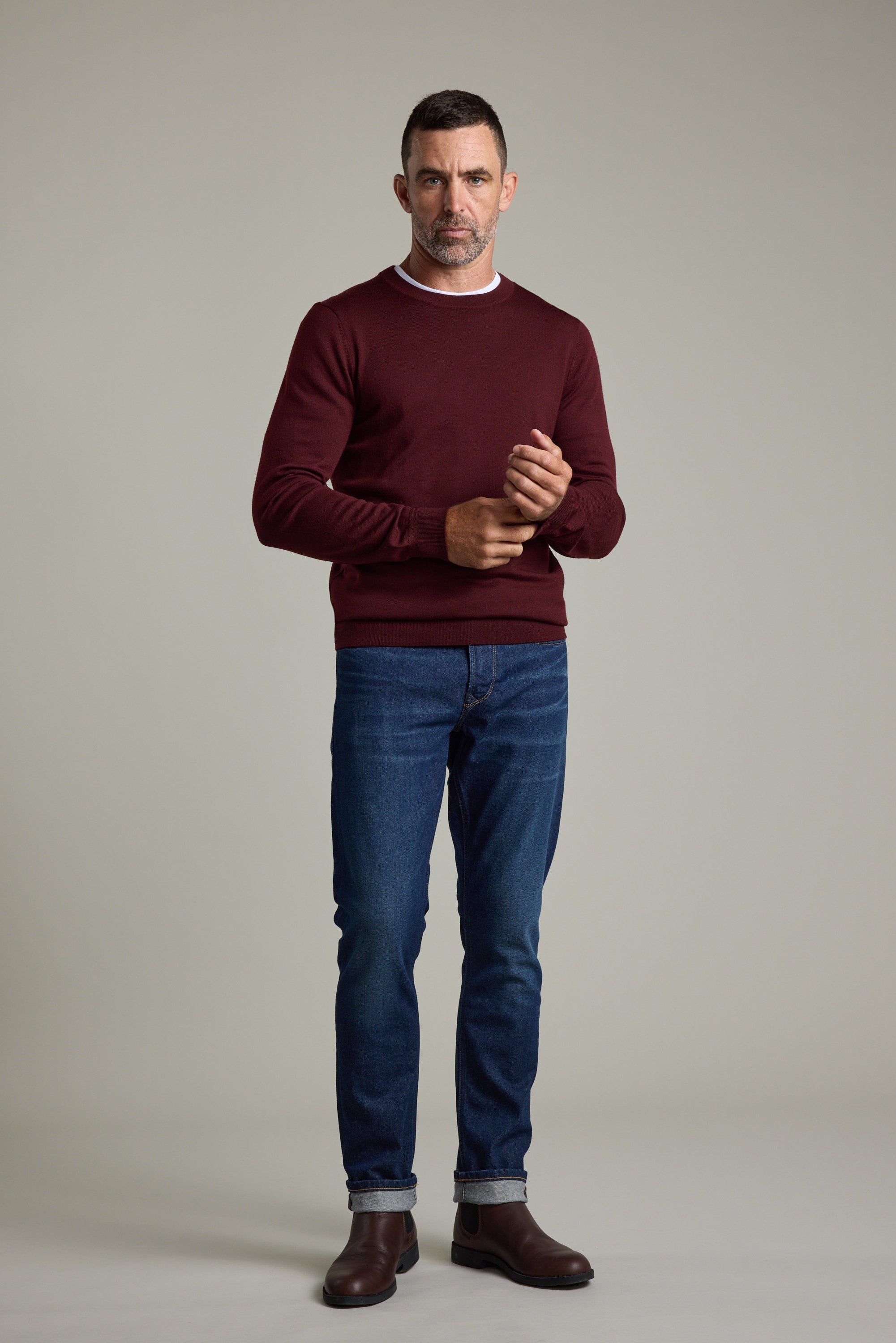 Man in a Barkers Skyland ZQrx Merino Crew, blue jeans, and brown boots against a plain background.