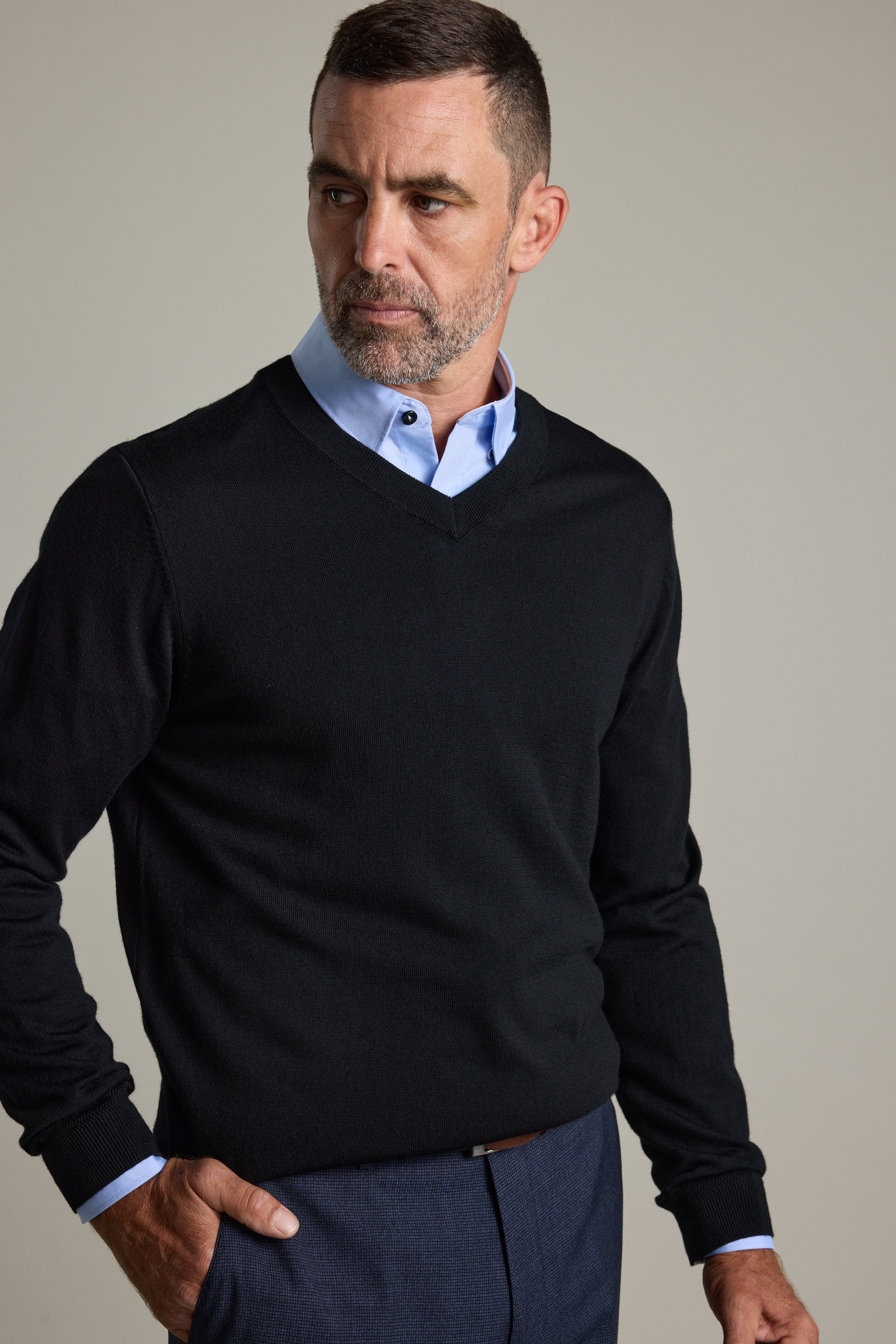 Man wears Barkers Skyland ZQrx Merino Vee sweater over a blue shirt against plain background.