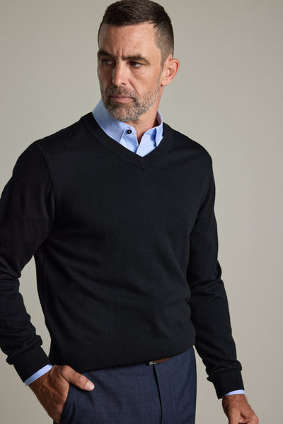 Man wears Barkers Skyland ZQrx Merino Vee sweater over a blue shirt against plain background.