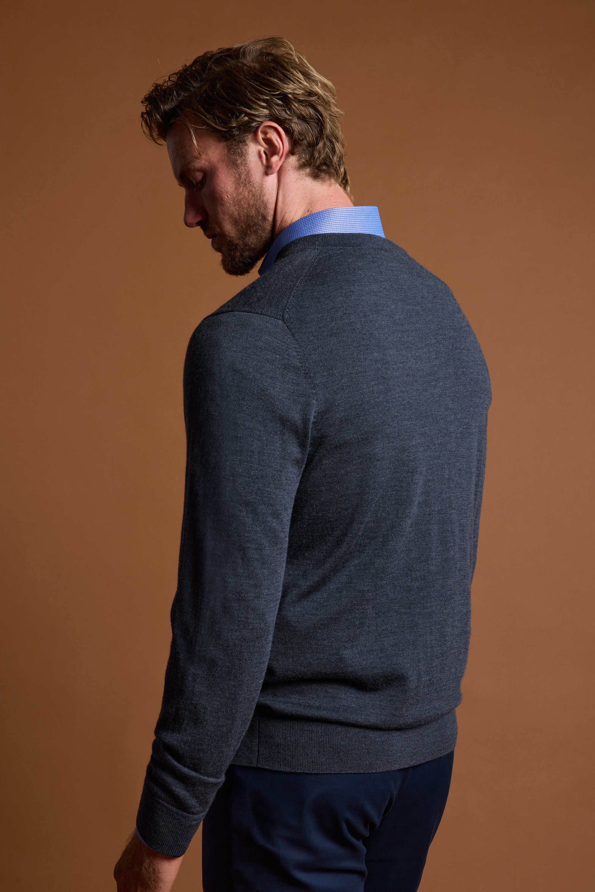 Man in Barkers Skyland ZQrx Merino Vee sweater stands against a brown background.