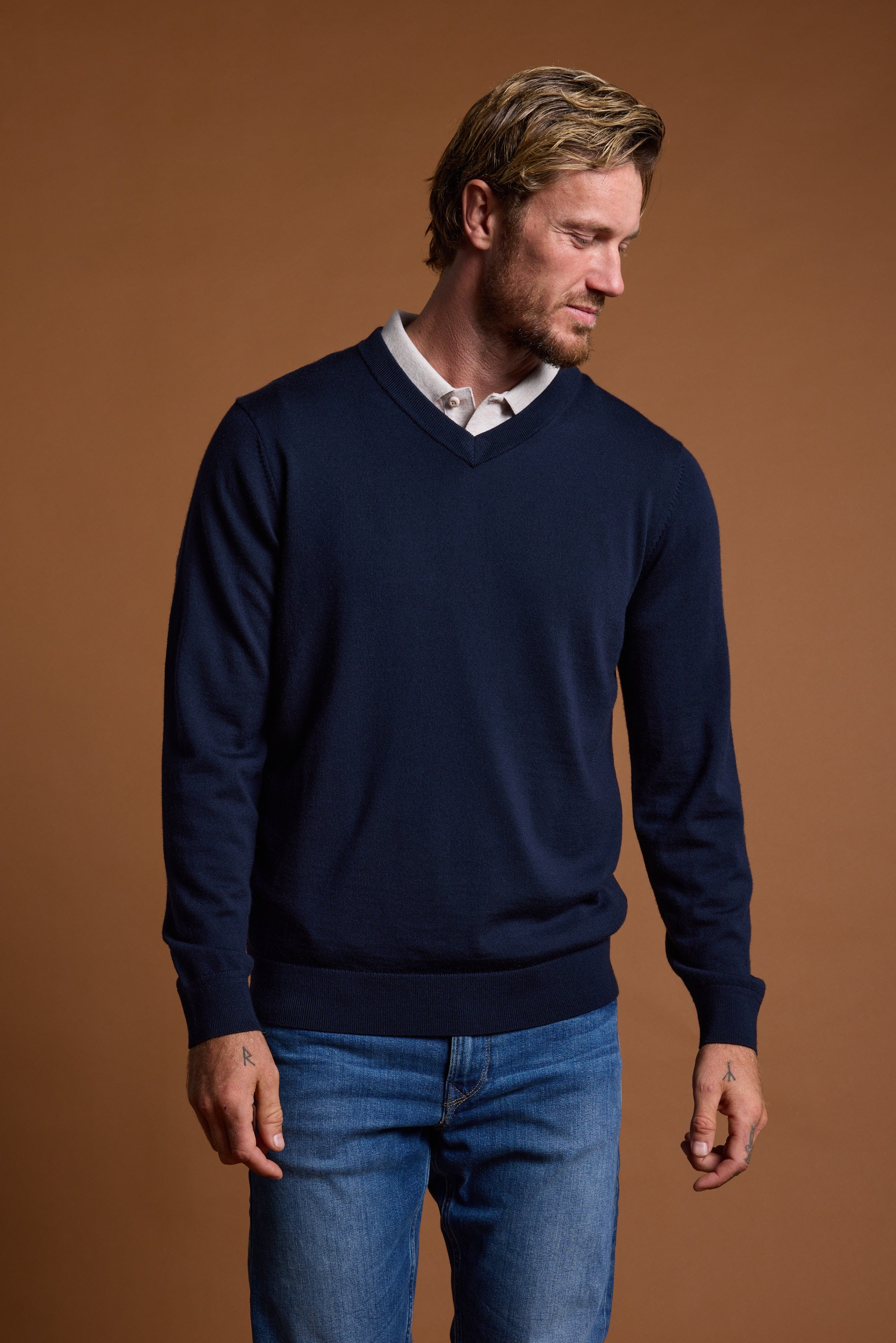 Man in a Barkers Skyland ZQrx Merino Vee sweater and jeans against a plain brown background.