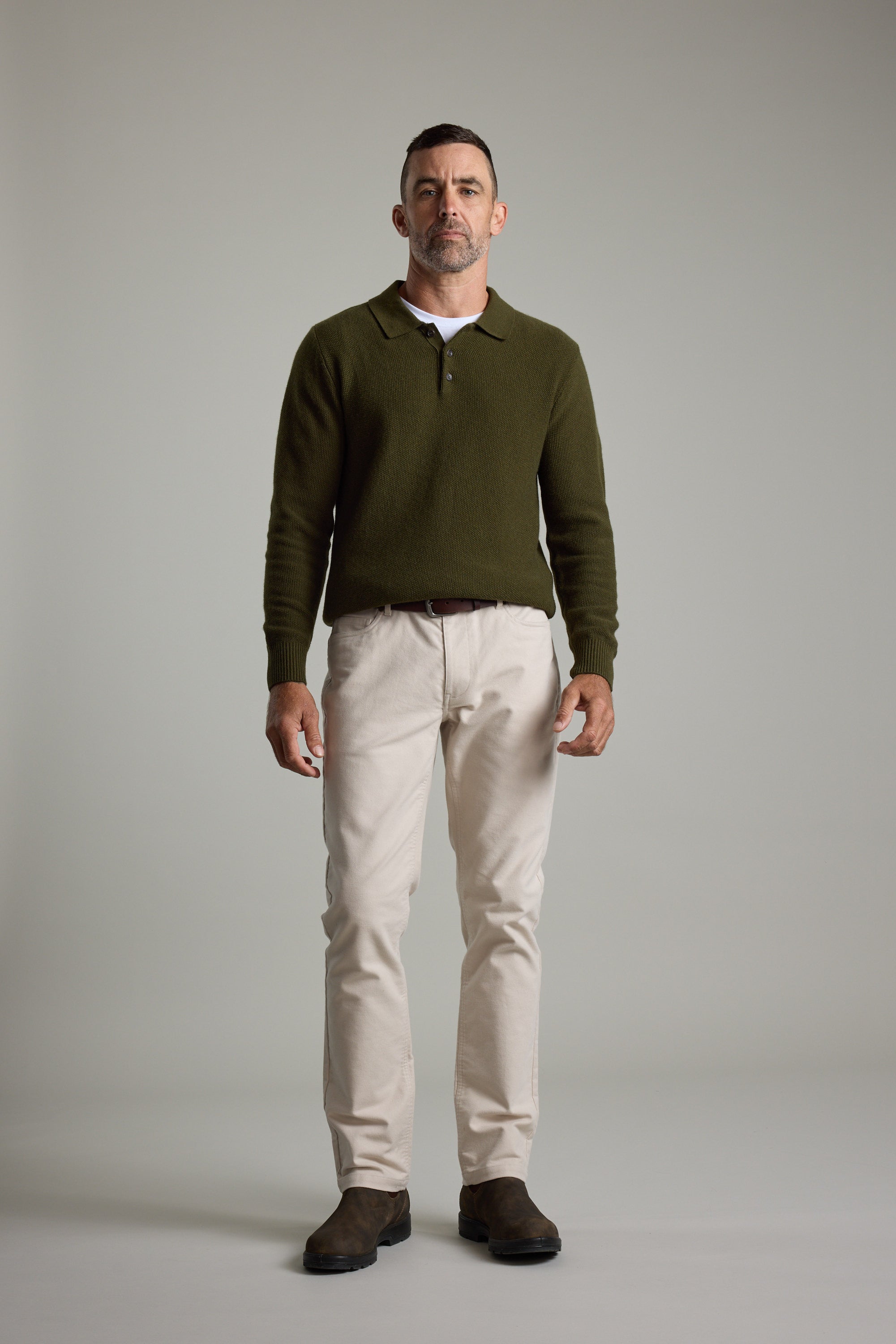 Man in studio wears Barkers Ainsley Woollen Long Sleeve Polo, beige pants, and brown shoes.