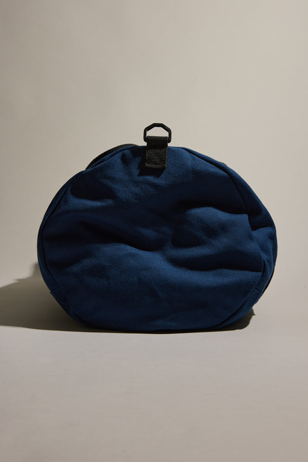 The Barkers Canvas Duffle Bag, round and blue with a black top strap, stands upright against a neutral background—your ideal travel companion from Barkers.