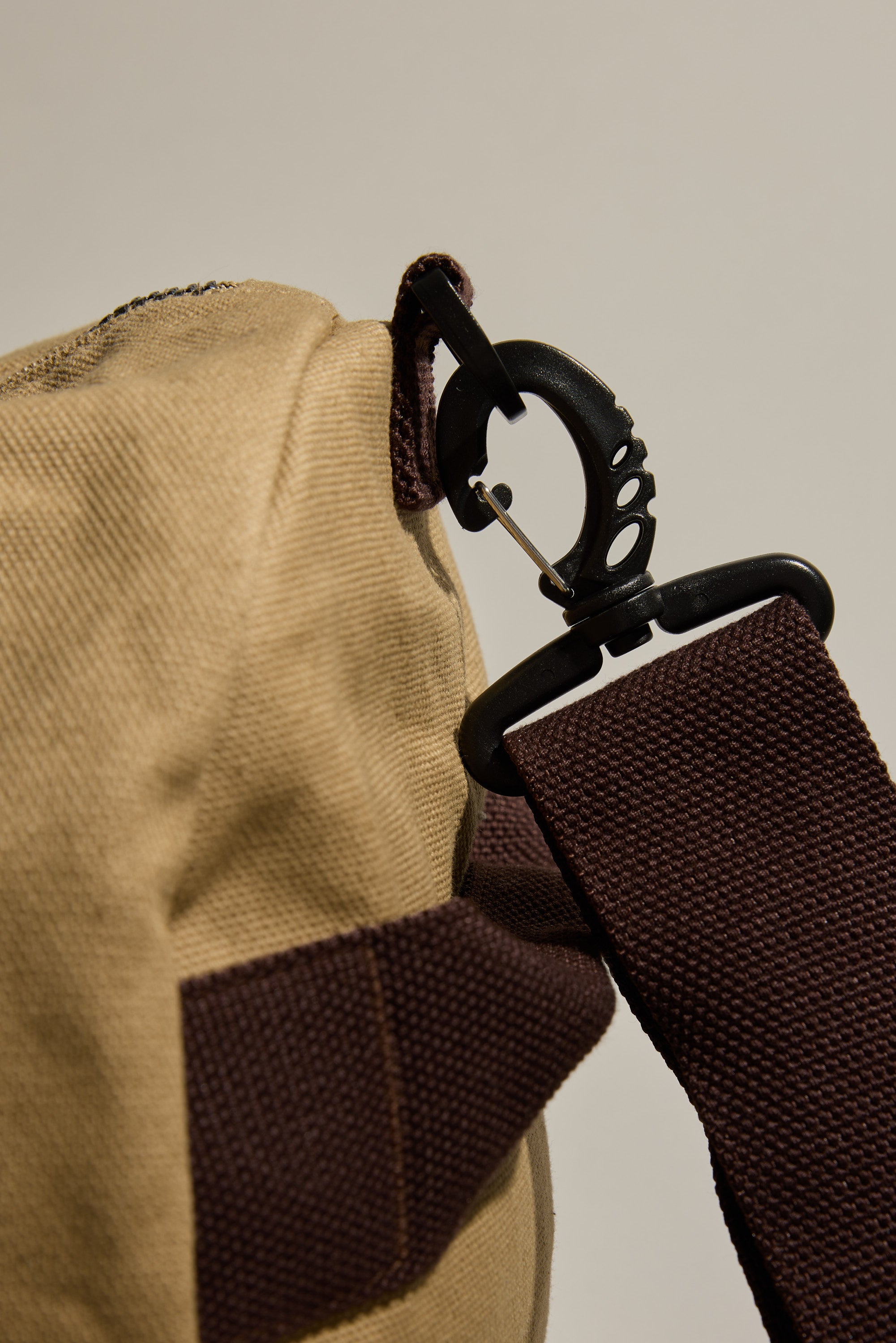 Close-up of a black plastic clip fastening a dark brown strap to the tan Barkers Canvas Duffle Bag by Barkers, making it an ideal travel companion against a plain light background.