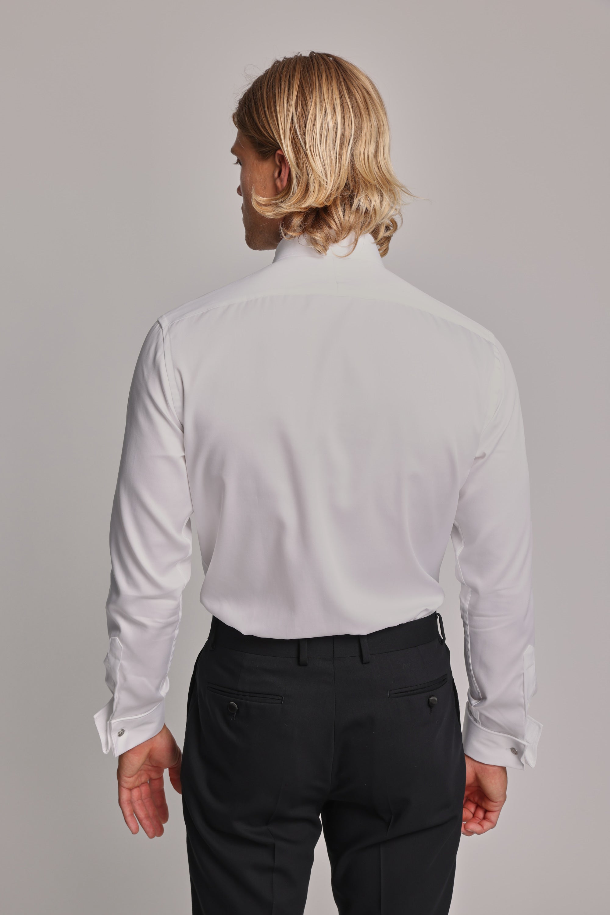 A person with shoulder-length blonde hair is seen from behind wearing the Barkers Eldridge Dress Shirt and black dress pants as formal wear against a plain light background.