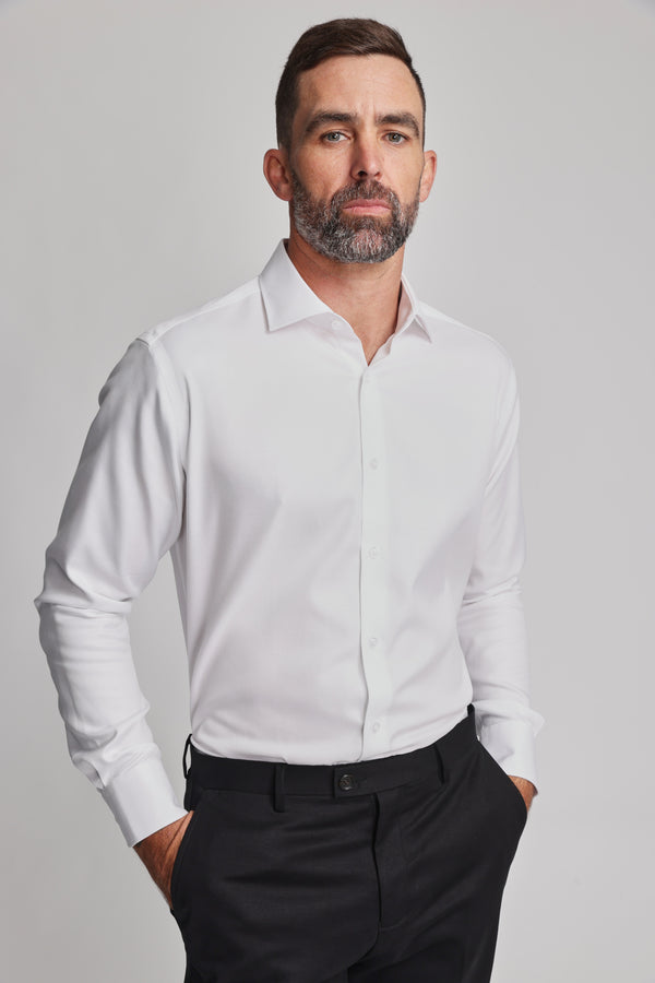 A man with short dark hair and a beard wears the Barkers Mexted Texture Shirt in white and black pants, standing with his hands in his pockets against a plain light background.