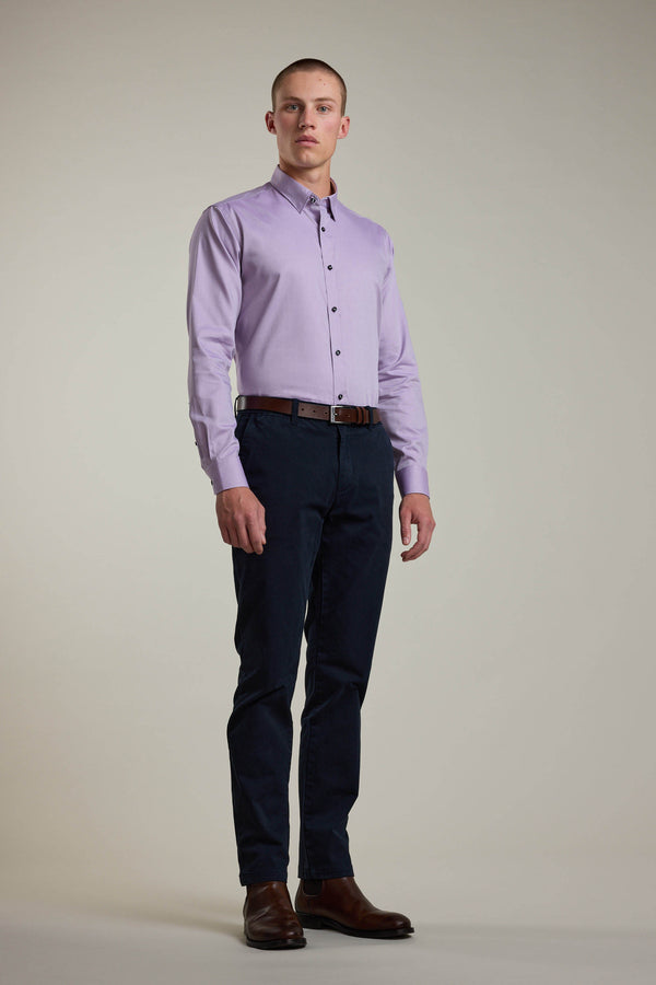A man stands against a plain background, wearing the Barkers Verona Shirt—a tailored fit, long sleeve, light purple 100% cotton business shirt—paired with dark blue pants, a brown belt, and brown shoes.