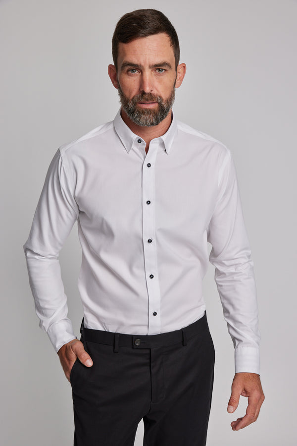 A man with short brown hair and a beard wears the Barkers Verona Shirt, a tailored fit, long sleeve white business shirt in 100% cotton, paired with black pants, standing against a plain light gray background.