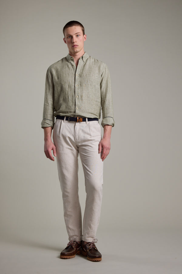 A man stands before a plain gray backdrop wearing the Barkers Dorset Linen Shirt in light green, tailored fit, paired with beige pants, a black belt, and brown shoes. His arms are by his sides and he has a neutral expression.