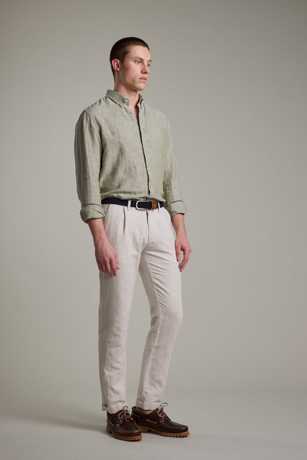 A man with short hair stands against a plain background in Barkers’ Dorset Linen Shirt, light green with rolled sleeves, tailored fit, paired with beige pants, a black belt, and brown shoes.