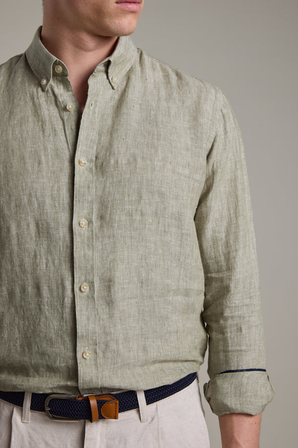 A man wears the Barkers Dorset Linen Shirt in light green with sleeves rolled up, paired with beige pants and a navy woven belt featuring brown leather accents. His face is partially visible against a neutral backdrop.