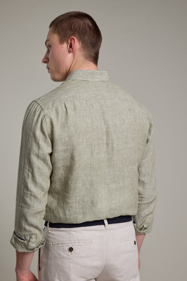 A person is shown from the back in a light green, tailored fit Dorset Linen Shirt by Barkers with beige pants, looking slightly left against a neutral background. The breathable fabric enhances its relaxed style.