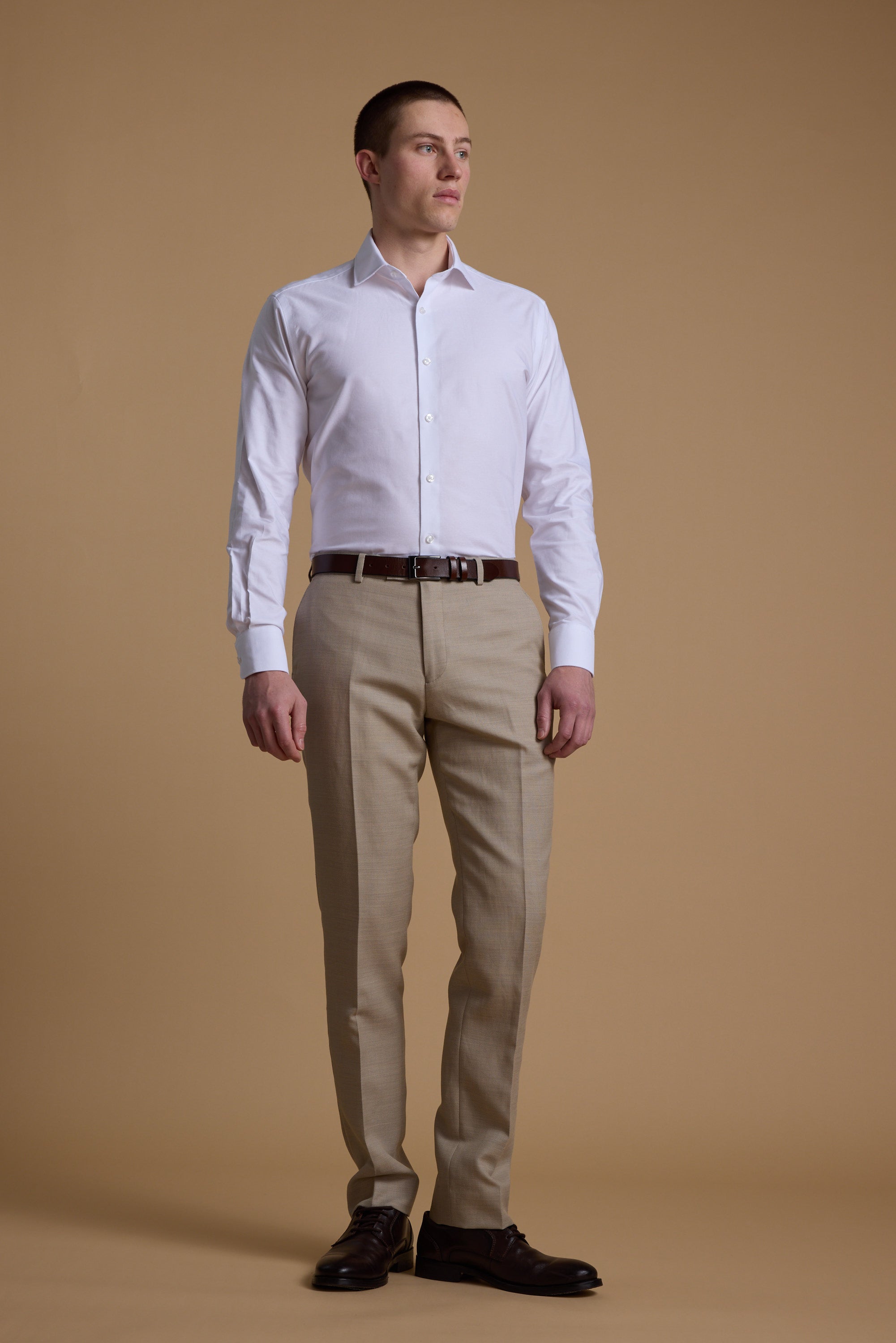Man in Barkers Aster Texture Business Shirt and beige pants stands before a brown backdrop.