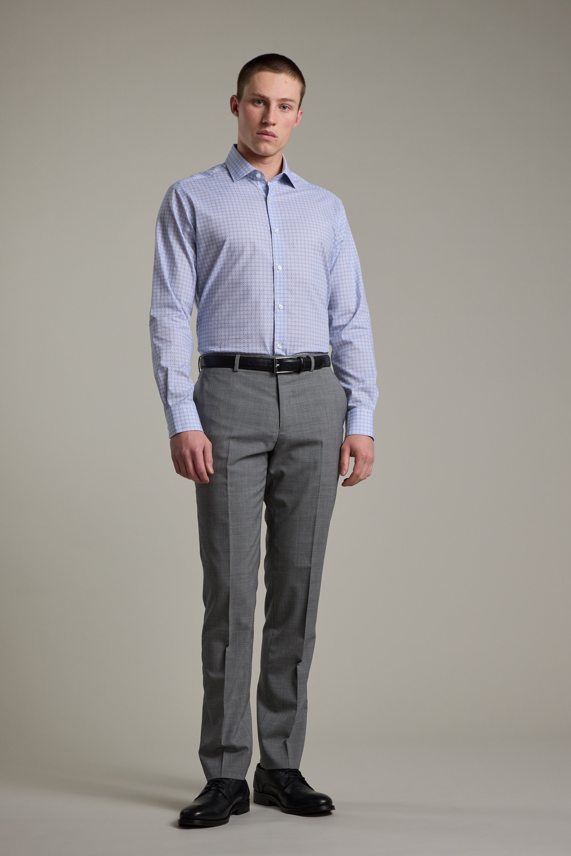 A man stands against a plain background wearing the Barkers Seton Print Business Shirt, paired with grey dress pants, a black belt, and black dress shoes. He faces the camera with a neutral expression.