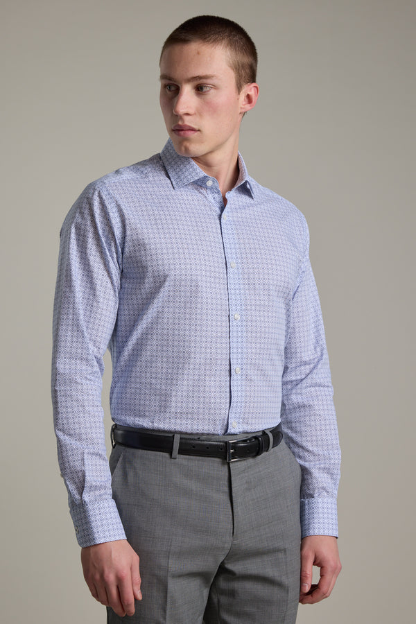 A man wearing the Barkers Seton Print Business Shirt in light blue stands against a plain background, paired with gray trousers and a black belt, looking to his left.