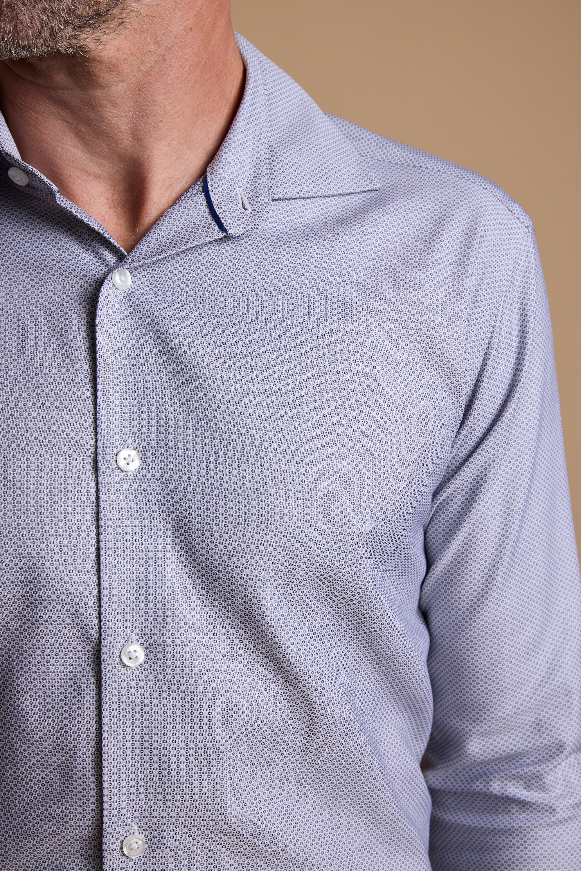 A close-up shows a man in the Barkers Eaton Jacquard Business Shirt, featuring a light blue pattern and spread collar. The shot, cropped at the mouth and mid-torso, is set against a plain beige background.