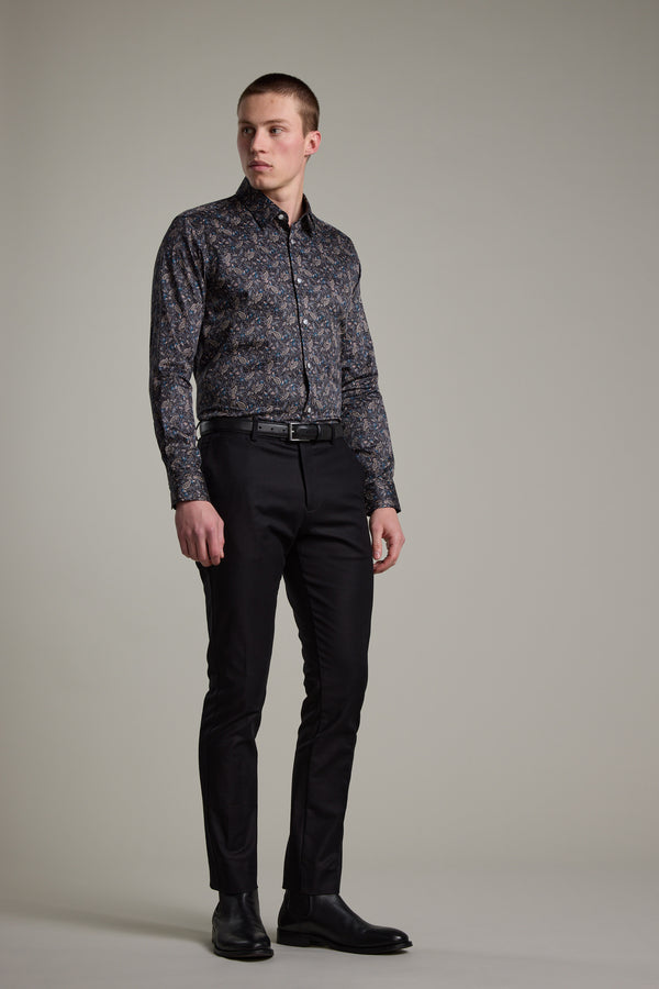 A man stands against a plain background wearing the Barkers Hilton Print Shirt, tucked into black fitted pants with a belt and black dress shoes. He looks slightly to the side with a neutral expression.