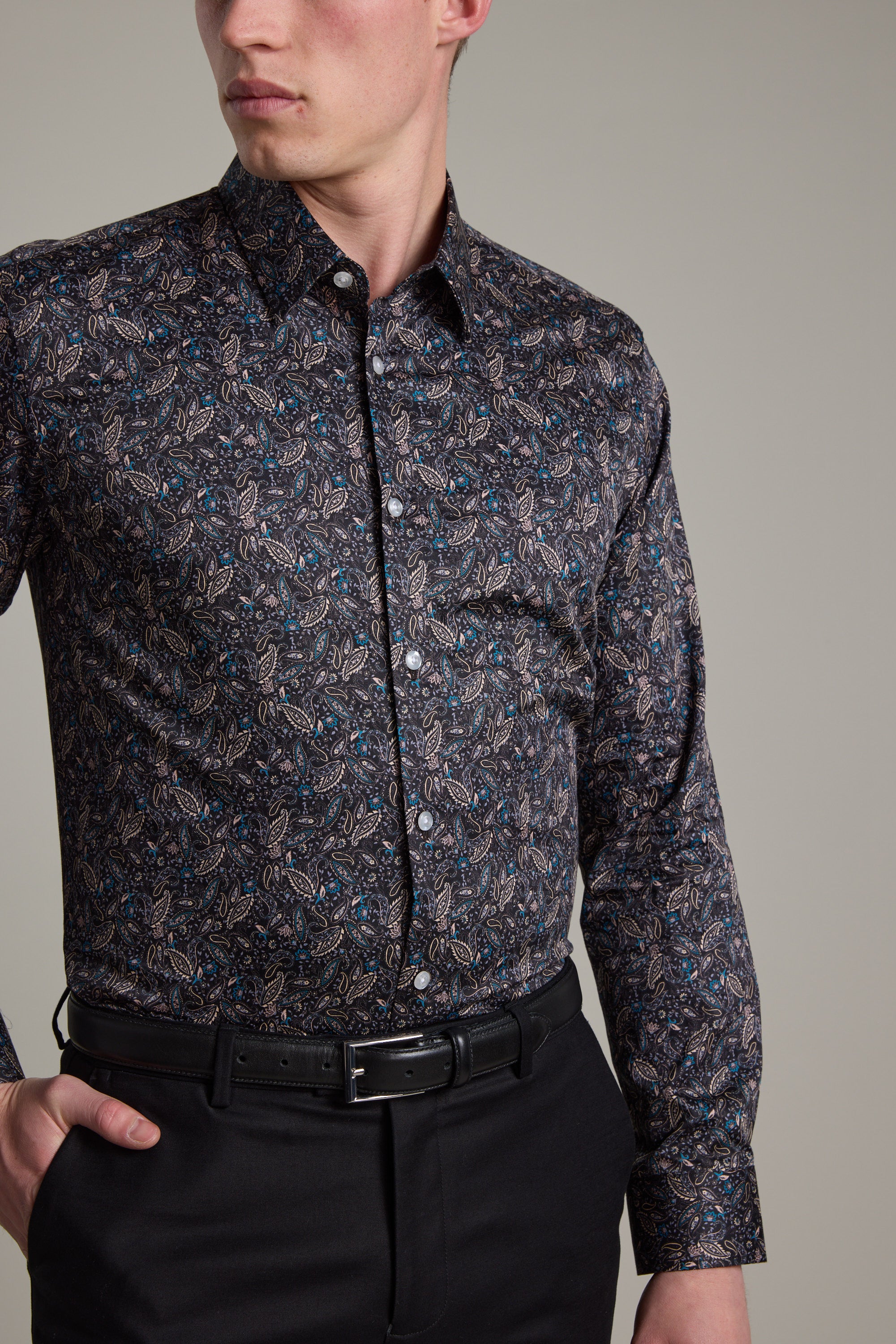 A man wears the Barkers Hilton Print Shirt, a tailored fit crafted from responsibly sourced cotton with a dark paisley pattern, paired with black dress pants and a belt. He stands against a plain light background with his left hand on his hip.