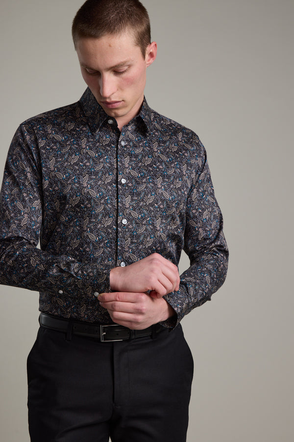 A man wearing the Barkers Hilton Print Shirt with a subtle floral pattern and black pants stands against a plain background, looking down as he adjusts his shirt cuff.
