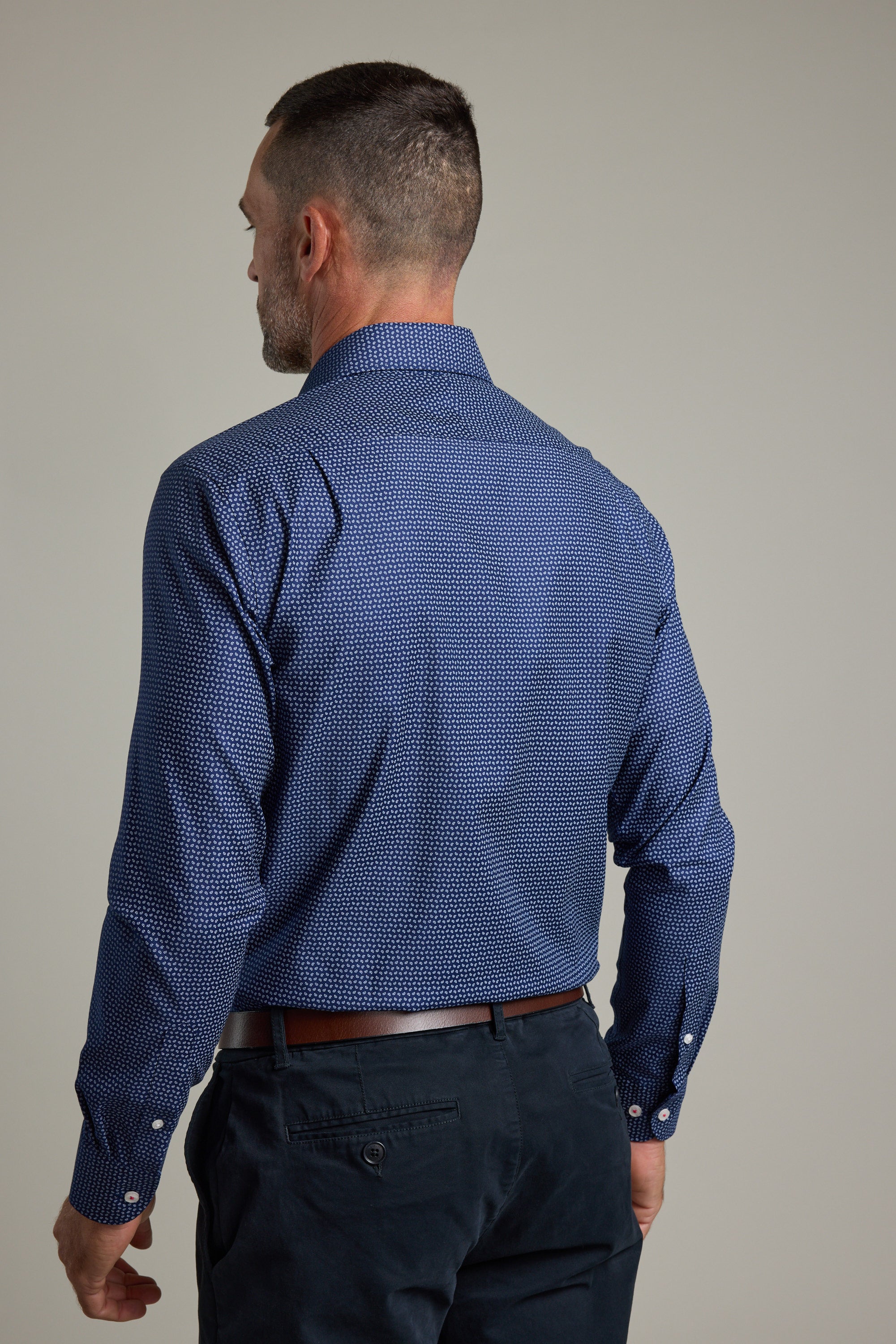 A man with short dark hair is shown from behind, wearing the Barkers Maiden Paisley Business Shirt in a tailored fit, paired with dark trousers. He stands against a plain light gray background.