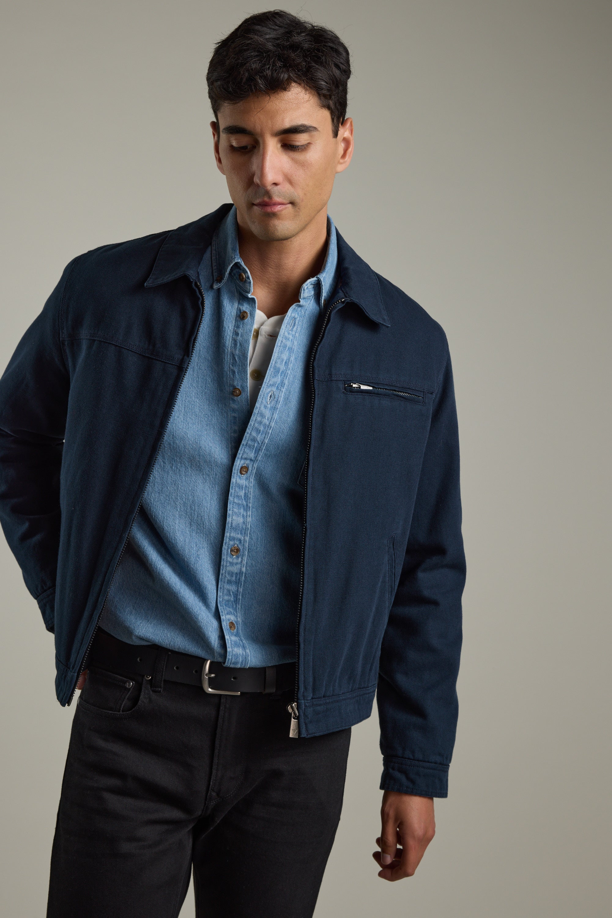 Man in Barkers Avalon Denim Shirt and blue jacket looking down against a neutral background.