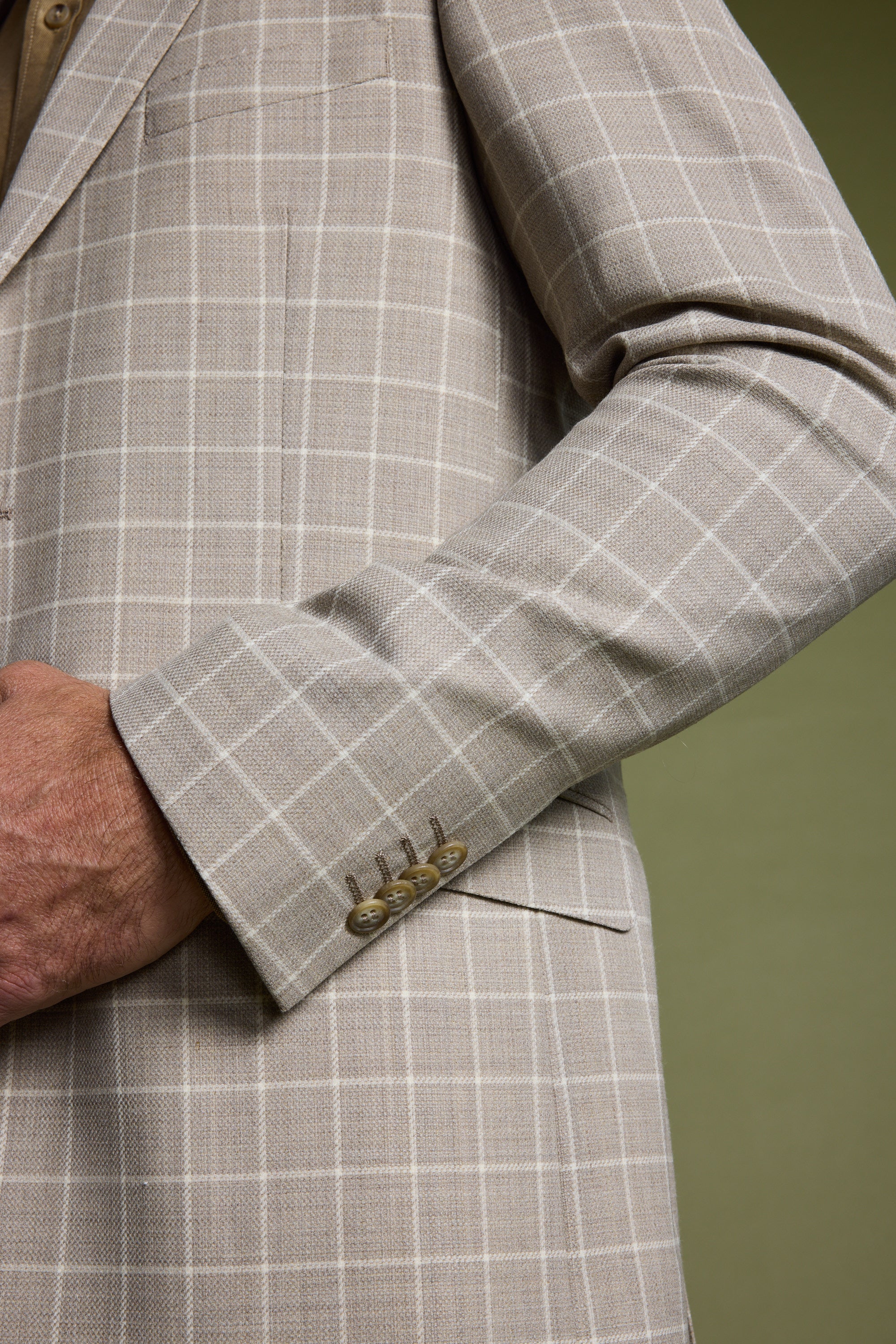 A close-up of a person wearing the Barkers Prestwick Check Blazer, featuring four buttons on the cuff, with part of their hand and arm visible against a plain green background.