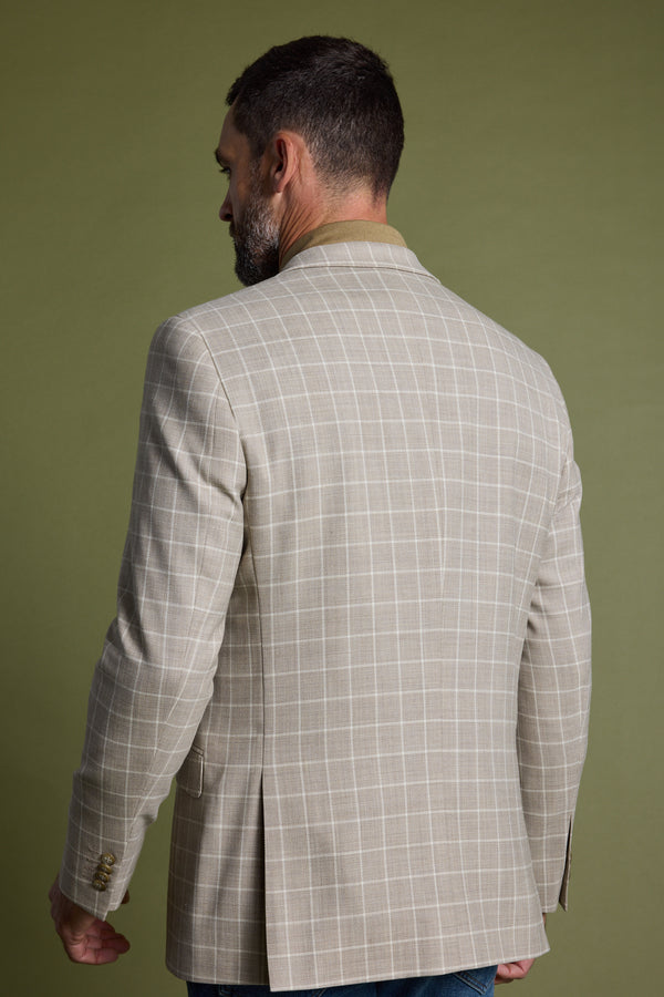 A man with short dark hair and a beard is seen from behind, wearing the Barkers Prestwick Check Blazer— a light beige, lightweight wool blazer with a subtle check pattern—perfect for summer events, against an olive green background.