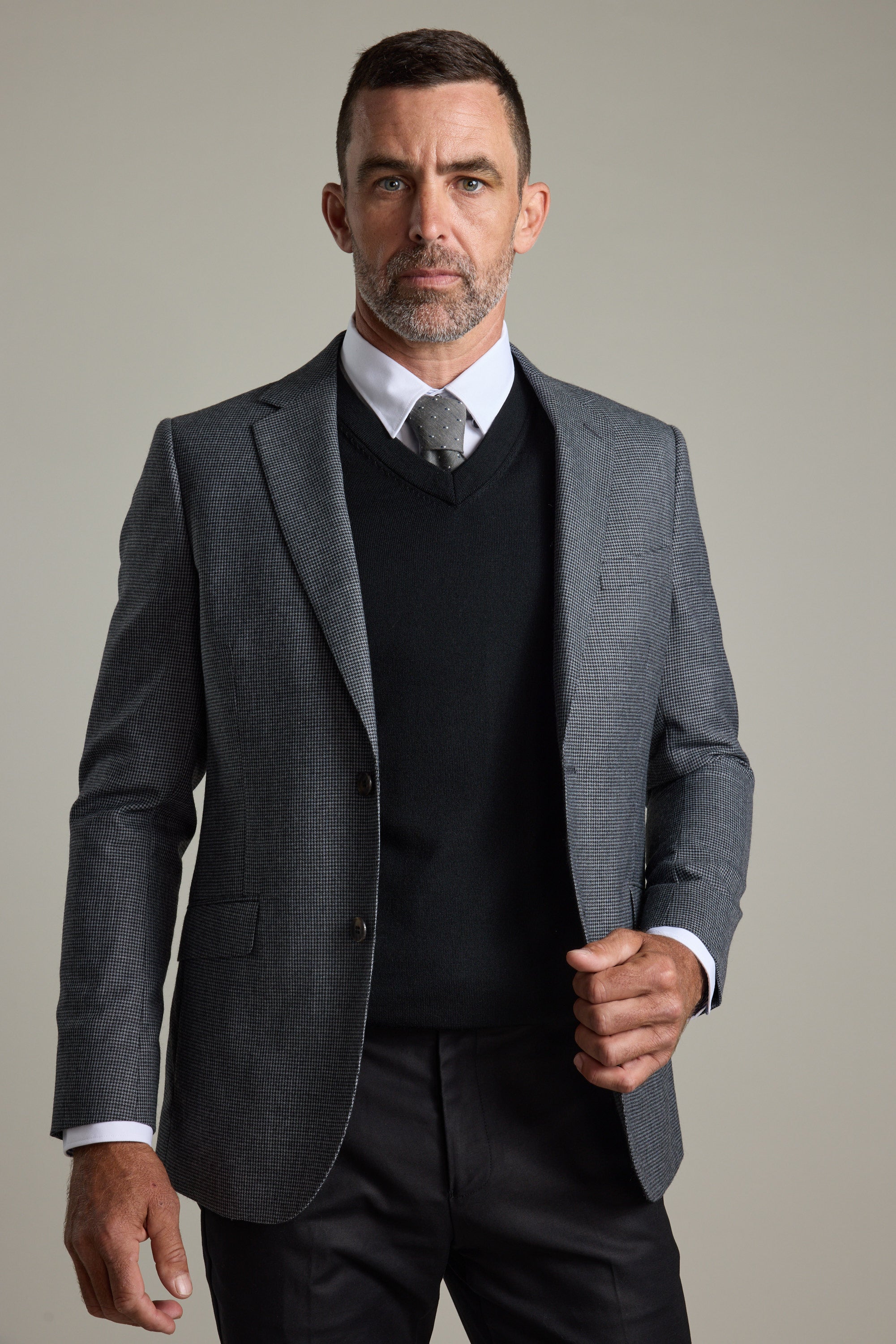 Man wears Barkers Skyland ZQrx Merino Vee sweater with suit and tie against plain background.