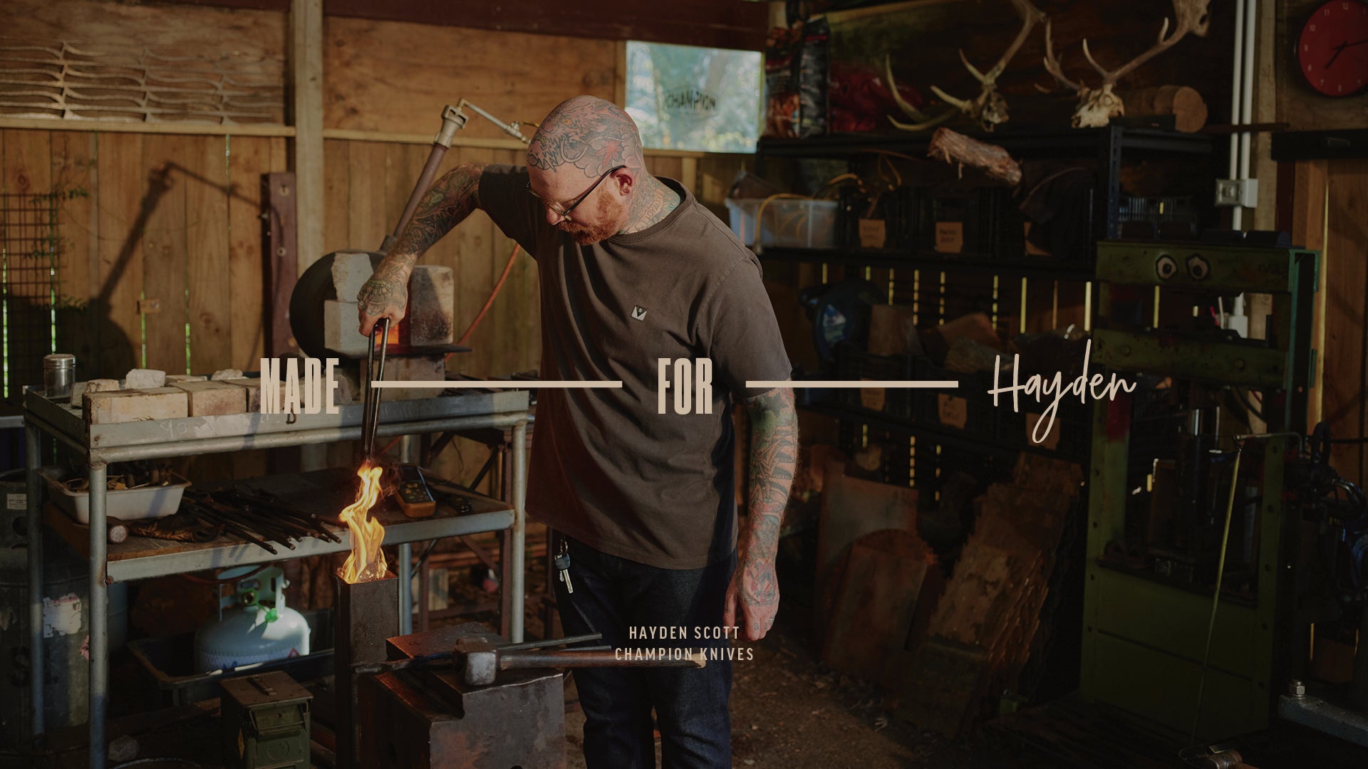 Tattooed NZ blacksmith working in a rustic workshop, forging metal over a flame.