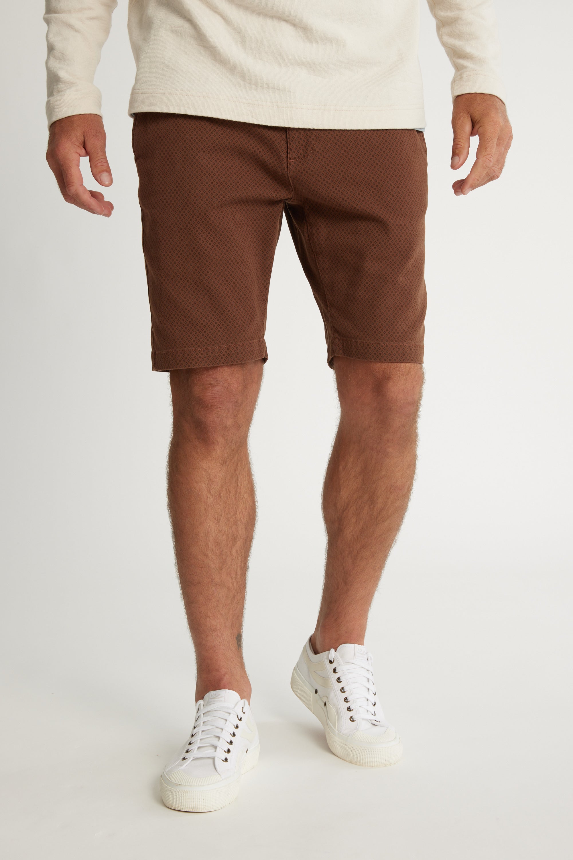 A man stands against a plain background wearing a cream long-sleeve shirt, Barkers Thomas GD Walk Shorts with a diamond print, and white sneakers. The image is cropped from the shoulders down.