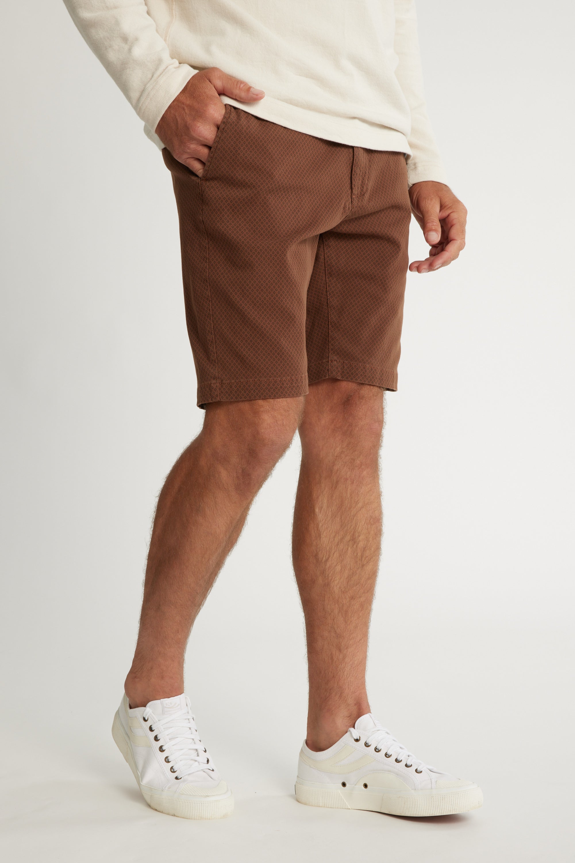 A person wears a cream long-sleeve shirt, Barkers Thomas GD Walk Short with diamond print, and white sneakers, standing with one hand in their pocket against a plain background. Only the body from shoulders down is shown.