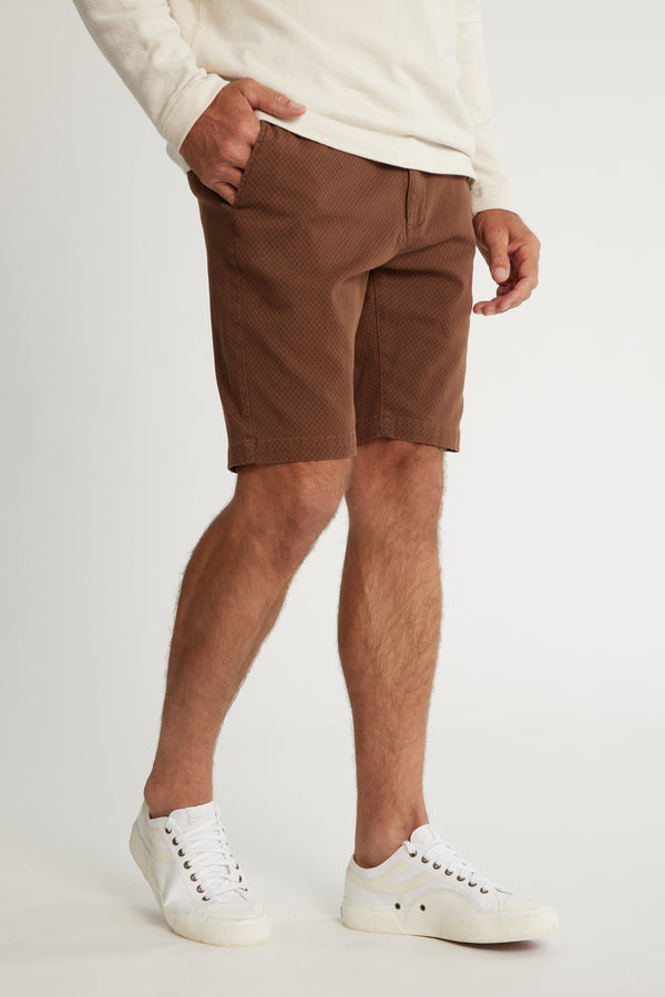A person wears a cream long-sleeve shirt, Barkers Thomas GD Walk Short with diamond print, and white sneakers, standing with one hand in their pocket against a plain background. Only the body from shoulders down is shown.