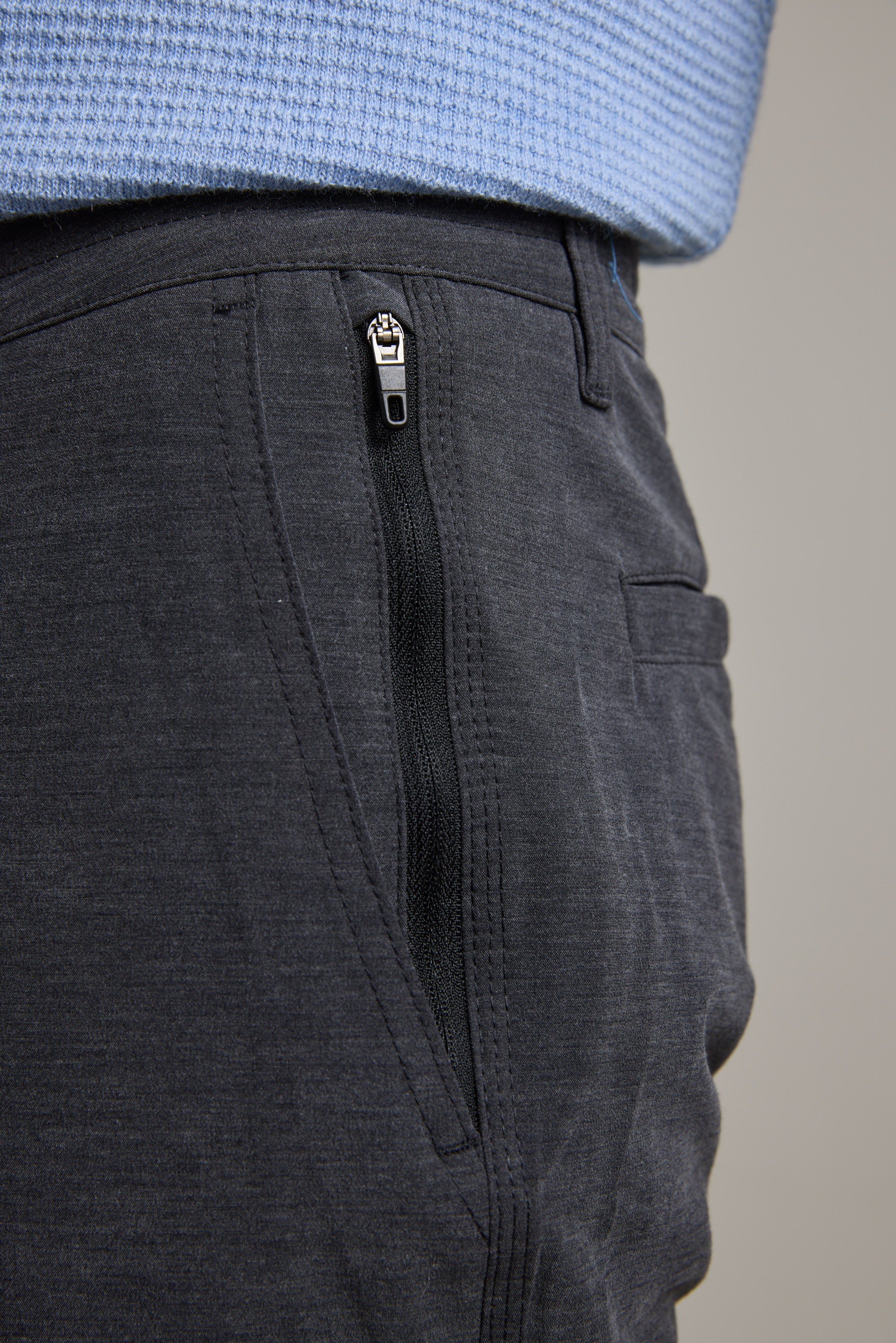 Close-up of a person wearing Barkers Hutchinson Walkshorts in dark gray four-way stretch fabric with a side zippered pocket, paired with a light blue textured knit sweater.