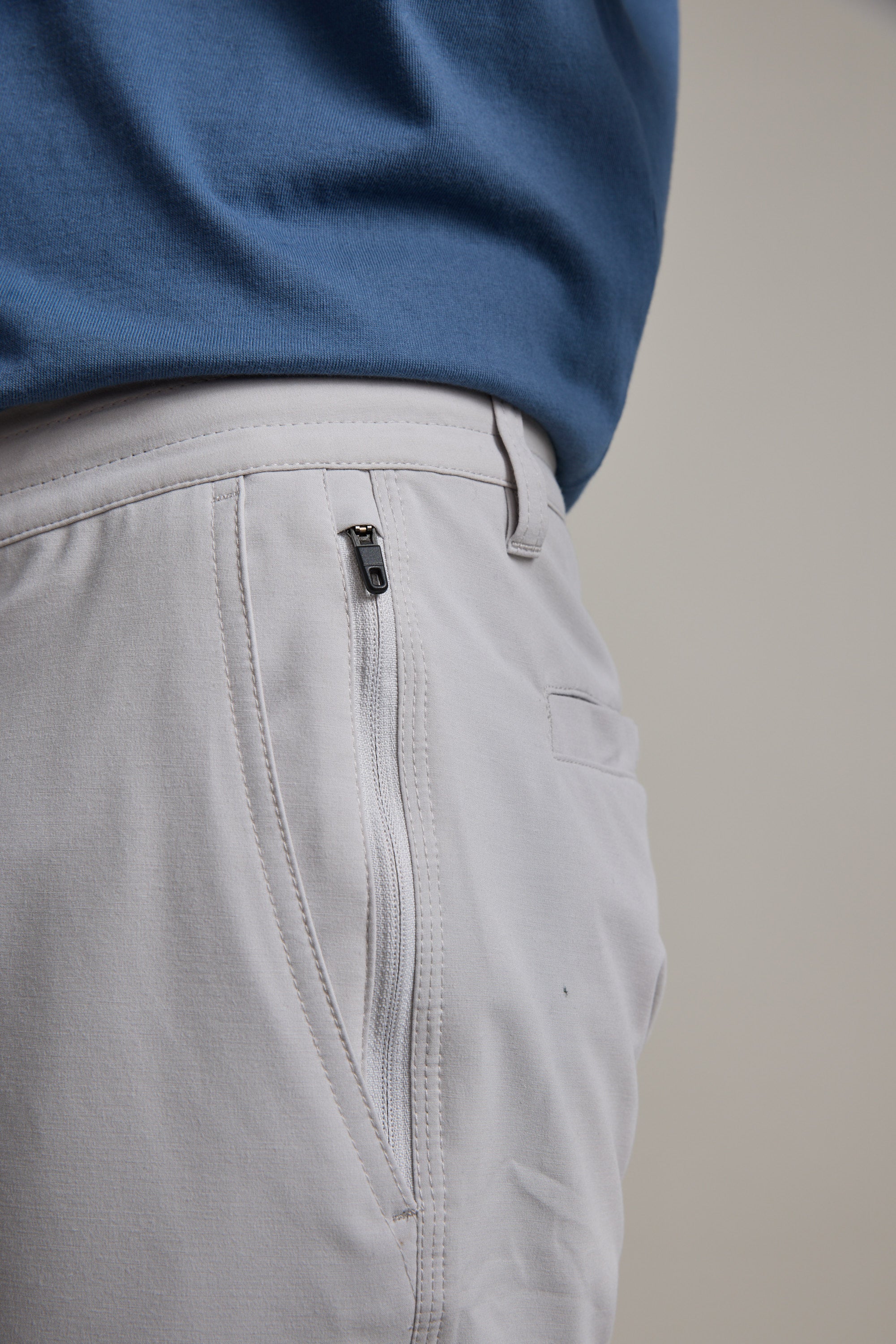 Close-up of a person wearing Barkers Hutchinson Walkshorts in light gray with a zipper pocket, paired with a tucked-in blue shirt. The image highlights the shorts' stitching and fabric around the waist and upper leg area.
