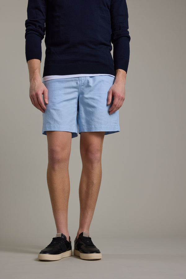 A person stands against a light background wearing Barkers' Jasper Linen Weekend Short, a navy sweater, white undershirt, and black sneakers with white soles. The image is cropped at the shoulders.