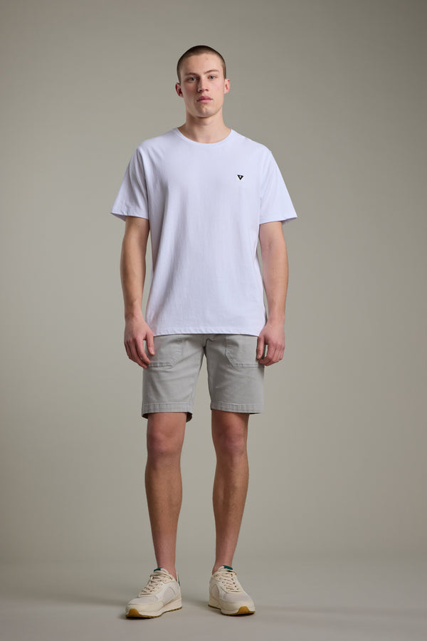 A young man stands against a plain background, wearing a white T-shirt, Barkers Tidal GD Utility Short in light gray, and beige sneakers. He faces forward with a neutral expression, arms relaxed at his sides.