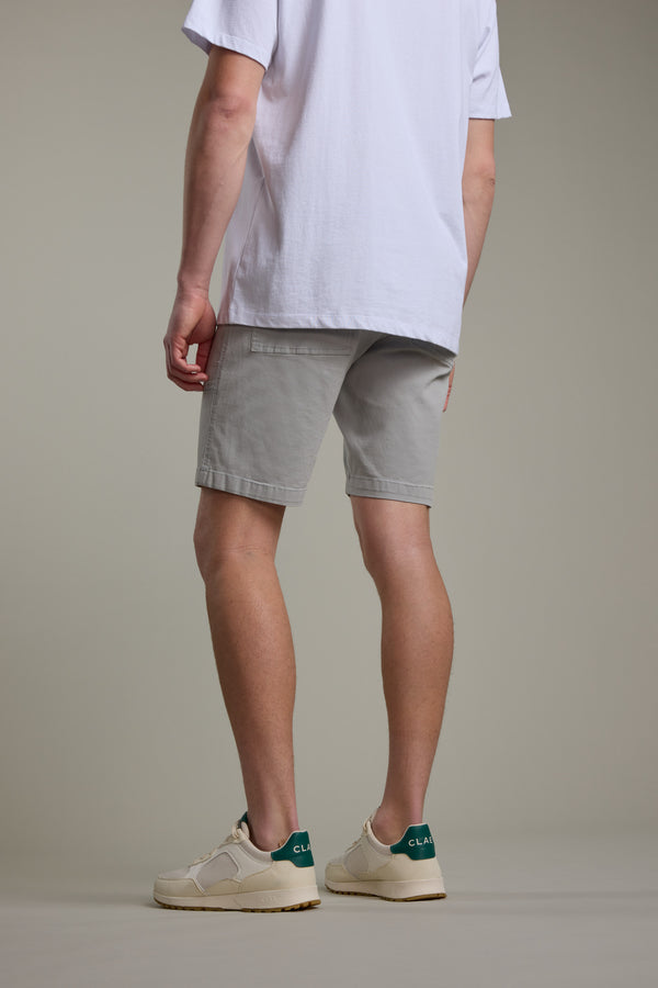 A person faces away wearing a white tee and Barkers Tidal GD Utility Short in light gray, paired with cream sneakers with green accents, set against a plain neutral background.